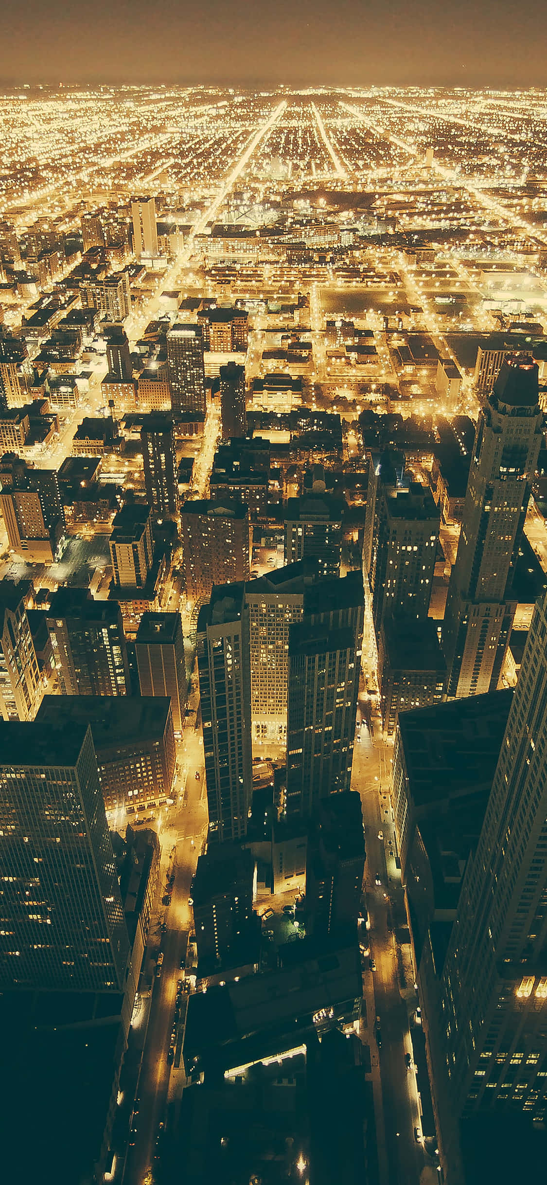 Chicago City Night 桌布 壁紙 — 夜晚廣闊城市的鳥瞰圖，金色燈光照亮摩天大樓和下方的街道。