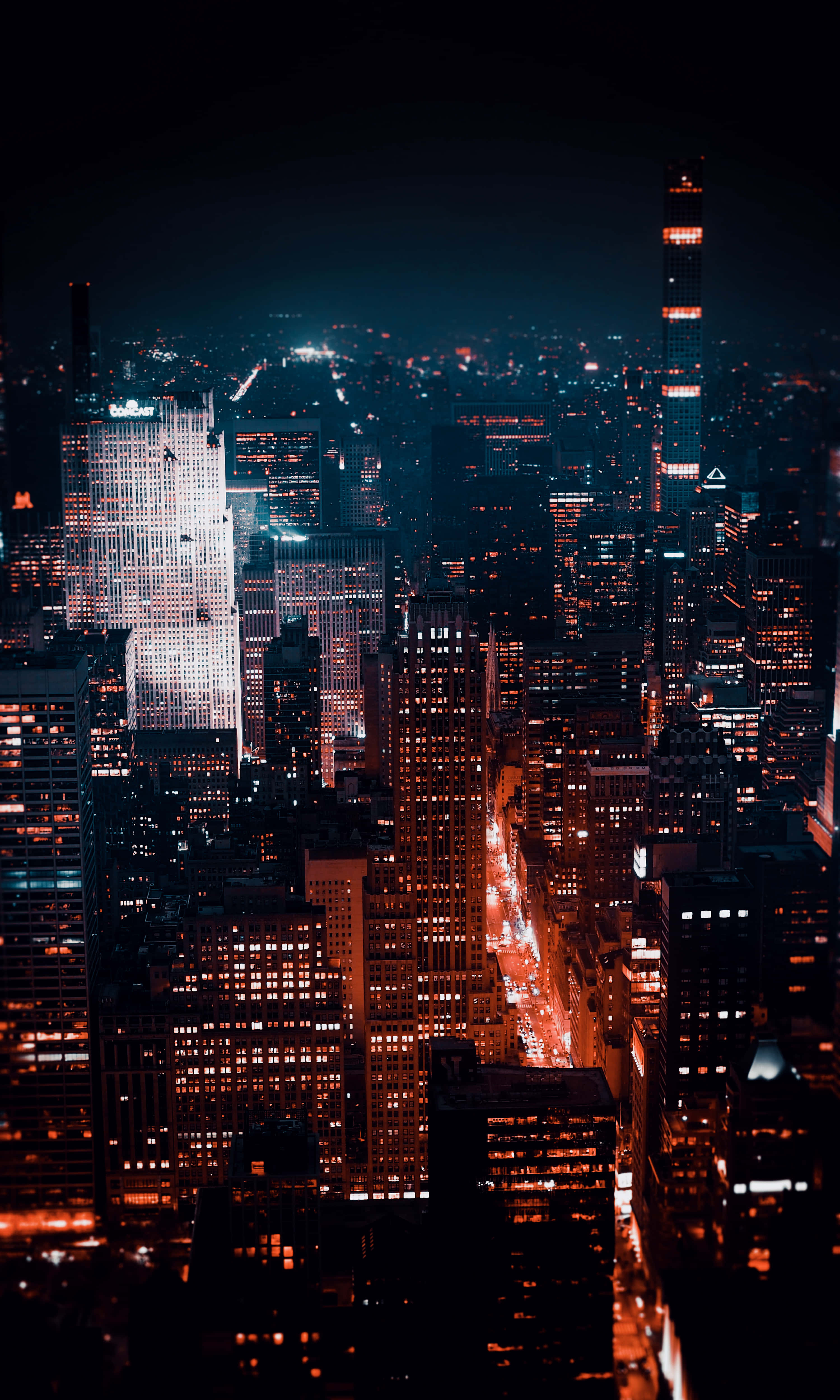 3d City 桌布 壁紙 — 夜晚廣闊城市的鳥瞰圖，閃爍的摩天大樓和充滿活力的橙色路燈照亮了城市峽谷。