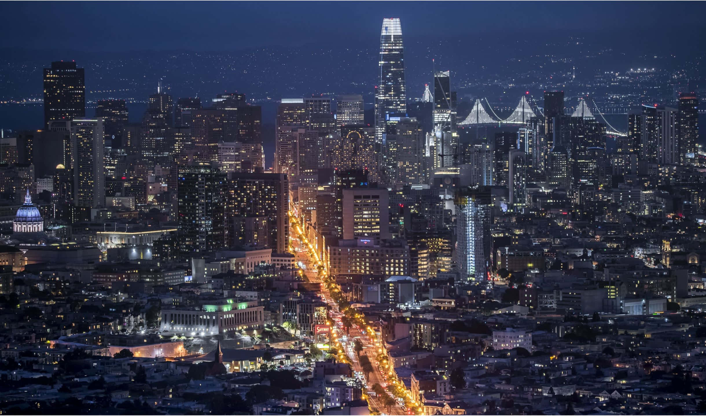 2440x1440 San Francisco 桌布 壁紙 — 夜晚廣闊城市的鳥瞰圖，閃爍的摩天大樓和一條充滿活力的照明街道延伸至遠方。
