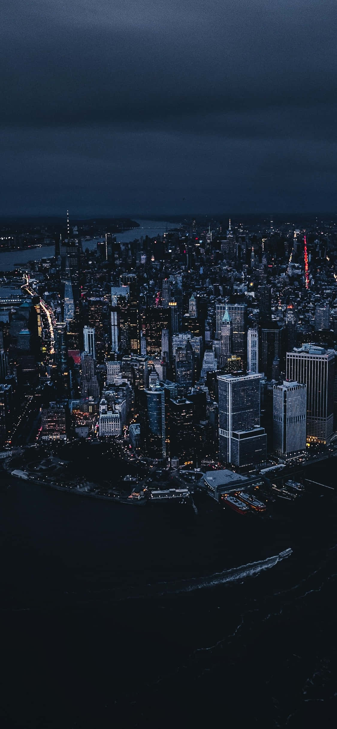 iPhone Xs New York 桌布 壁紙 — 夜晚廣闊城市的鳥瞰圖，閃爍的摩天大樓和黑暗的水面，在暴風雨的天空下。