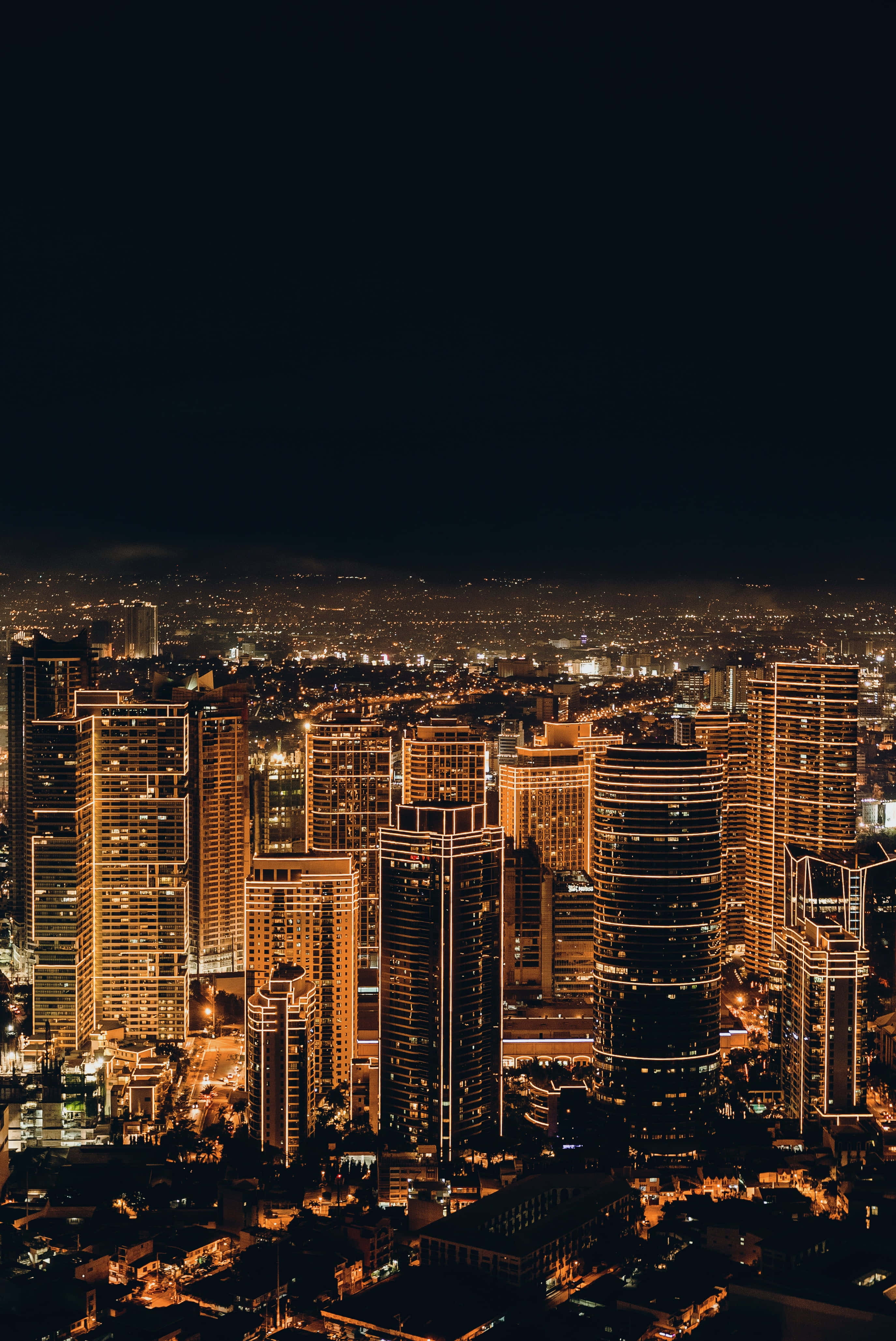 City Lights 桌布 壁紙 — 夜晚廣闊城市的鳥瞰圖，高聳的摩天大樓在黑暗的天空中溫暖地發光。