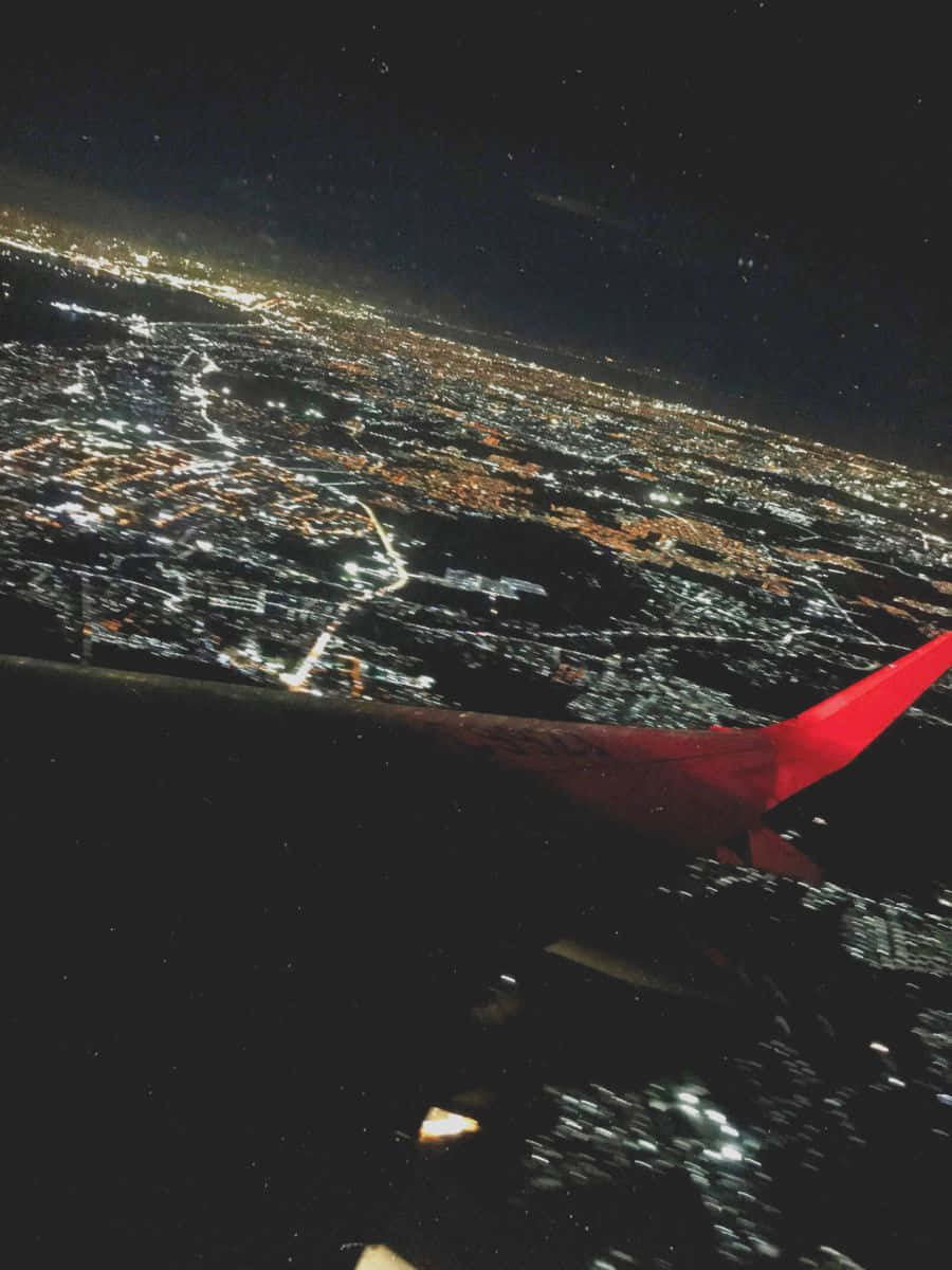 Airplane Window 桌布 壁紙 — 夜晚從空中俯瞰一座燈火通明的廣闊城市，前景是紅色的飛機機翼。