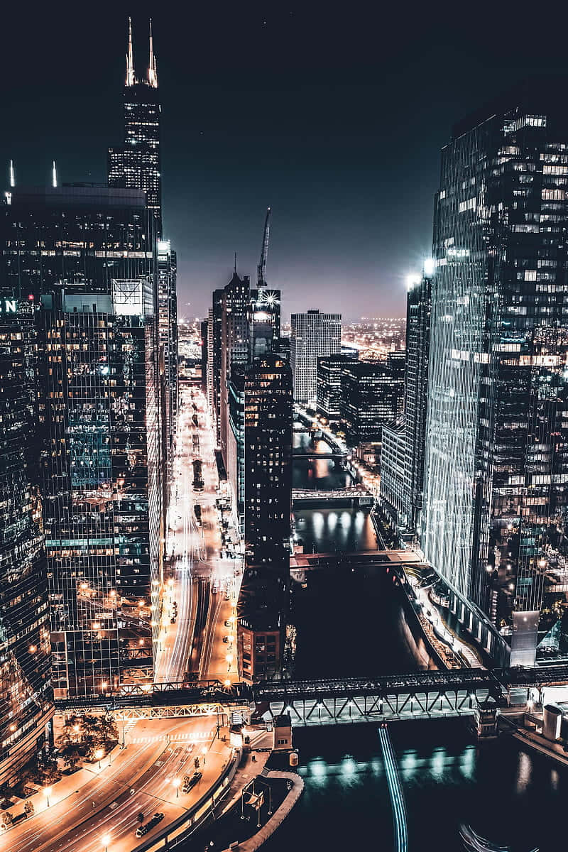 Chicago City Night 桌布 壁紙 — 夜晚從高空俯瞰充滿活力的城市景觀，高聳的摩天大樓在黑暗的天空中閃耀，河流反射著燈光。