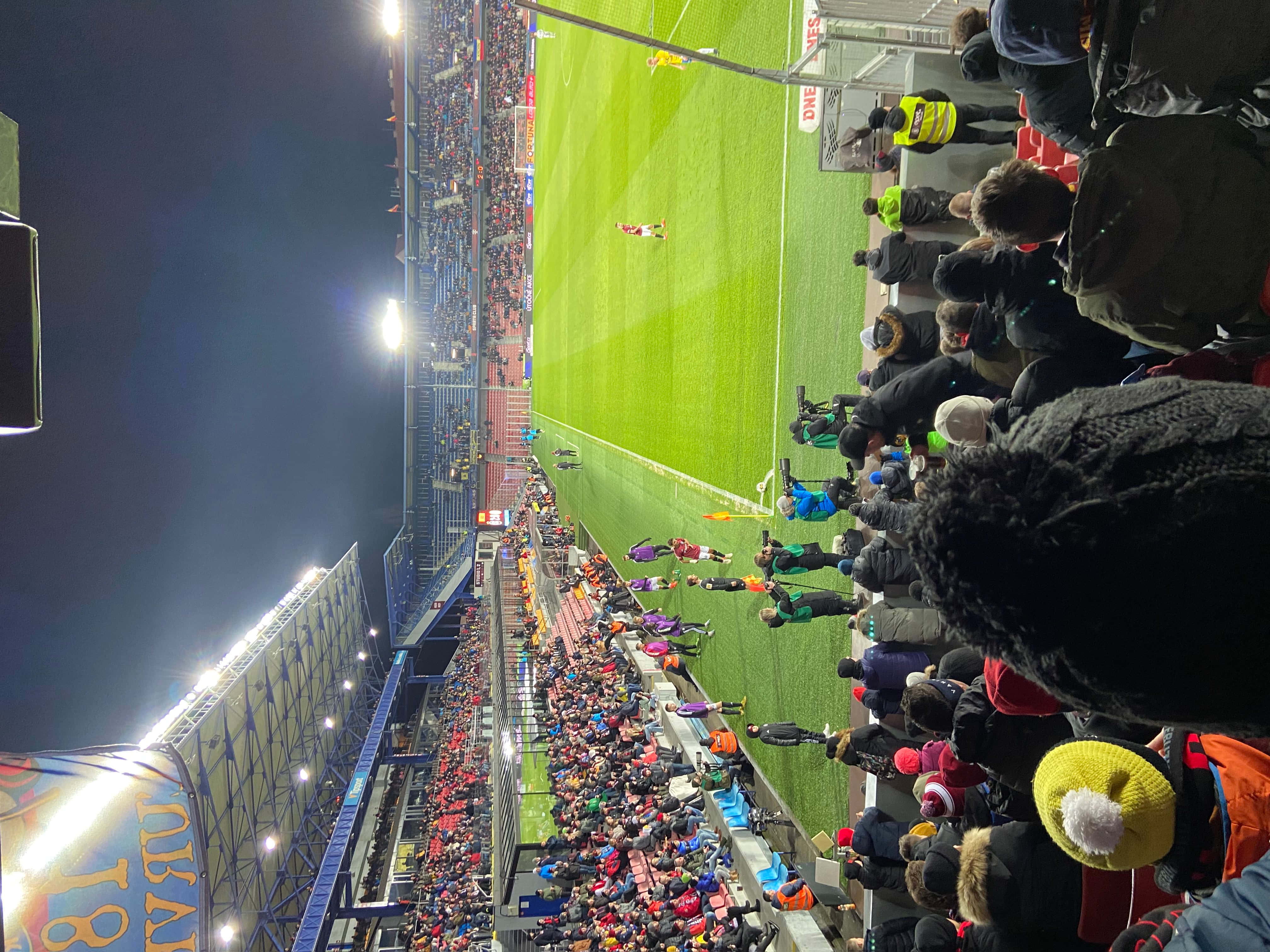 Corner Kick 桌布 壁紙 — 夜晚擠滿觀眾的足球場鳥瞰圖，明亮的泛光燈照亮了綠色球場和在看台上歡呼的球迷。
