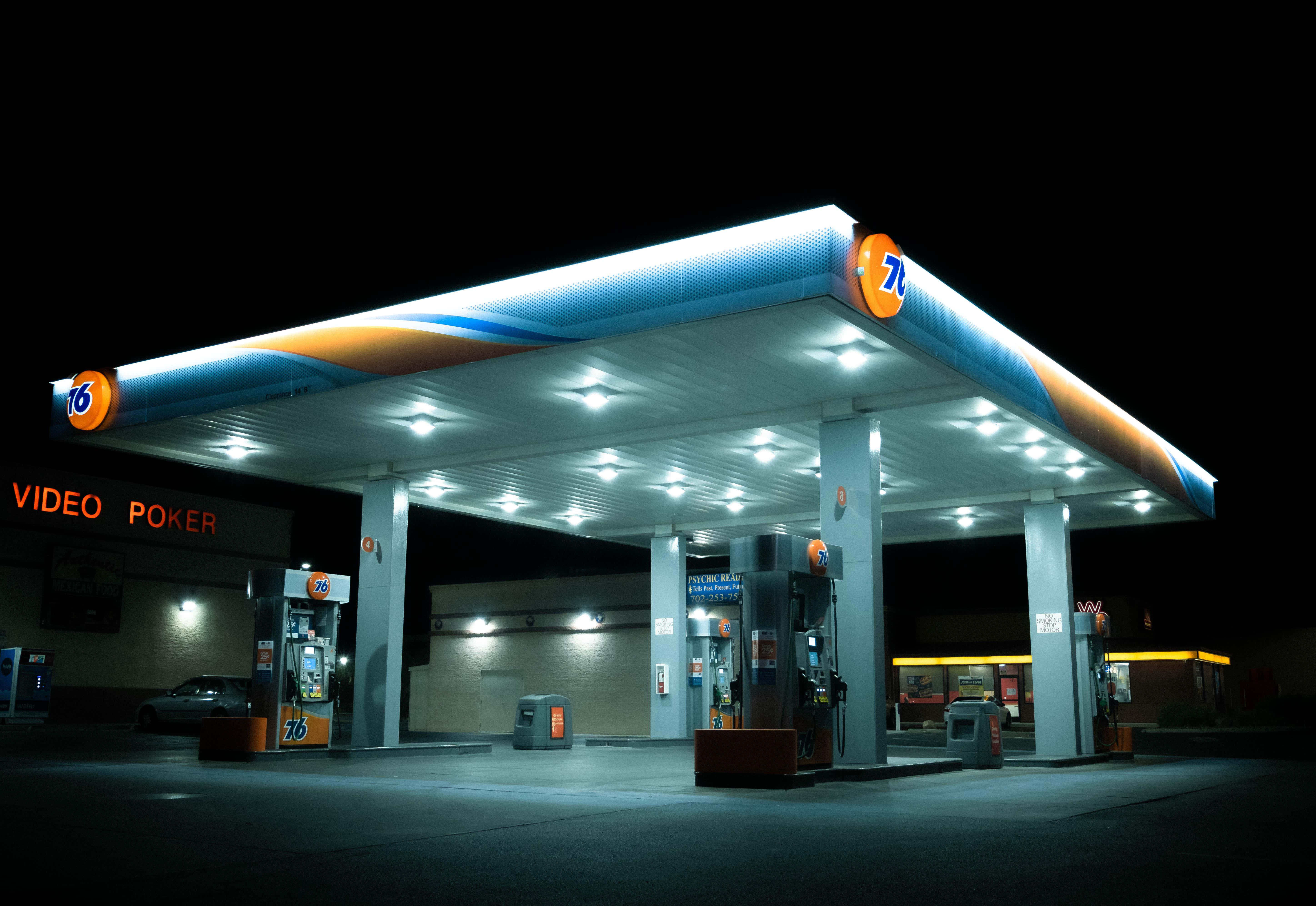Petrol Station 桌布 壁紙 — 夜晚明亮照明的76加油站頂篷，發光的油泵和黑暗中的視頻撲克牌標誌。