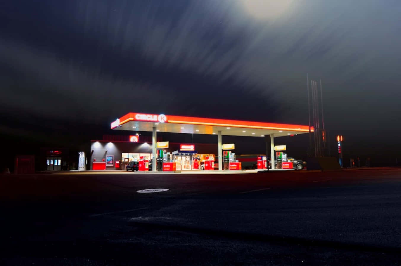 Petrol Station 桌布 壁紙 — 夜晚明亮照明的Circle K加油站，上方有條紋雲，前景是空蕩蕩的瀝青路面。