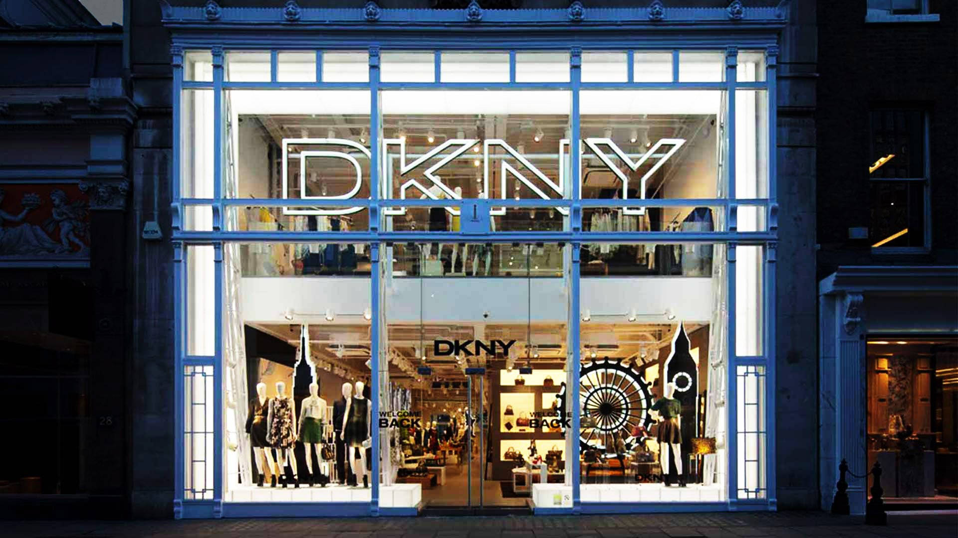 品牌 桌布 壁紙 — 夜晚明亮照明的DKNY商店，模特兒展示時尚陳列，發光招牌映襯著黑暗的城市街道。