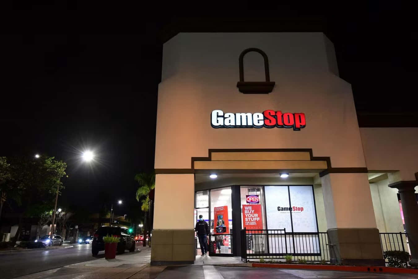 GameStop 桌布 壁紙 — 夜晚明亮照明的GameStop商店，有人在發光招牌下進入，街燈照亮人行道。