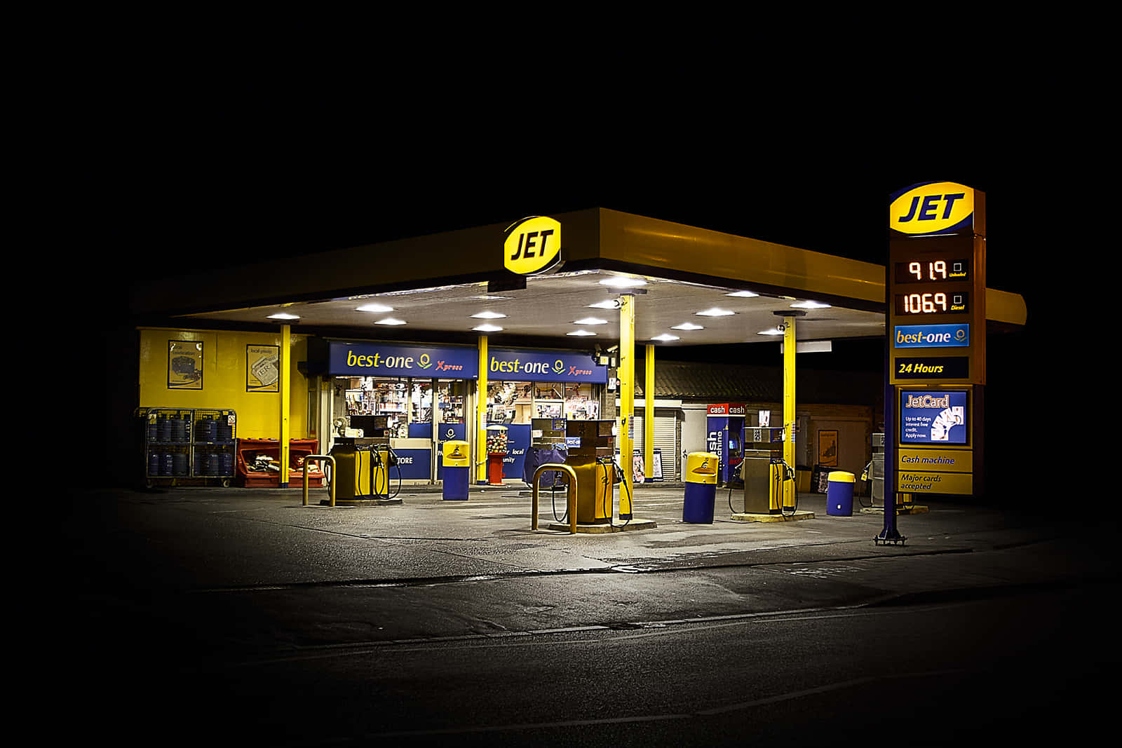 Petrol Station 桌布 壁紙 — 夜晚明亮照明的JET加油站，黃色油泵和發光標誌映襯著黑暗的天空。