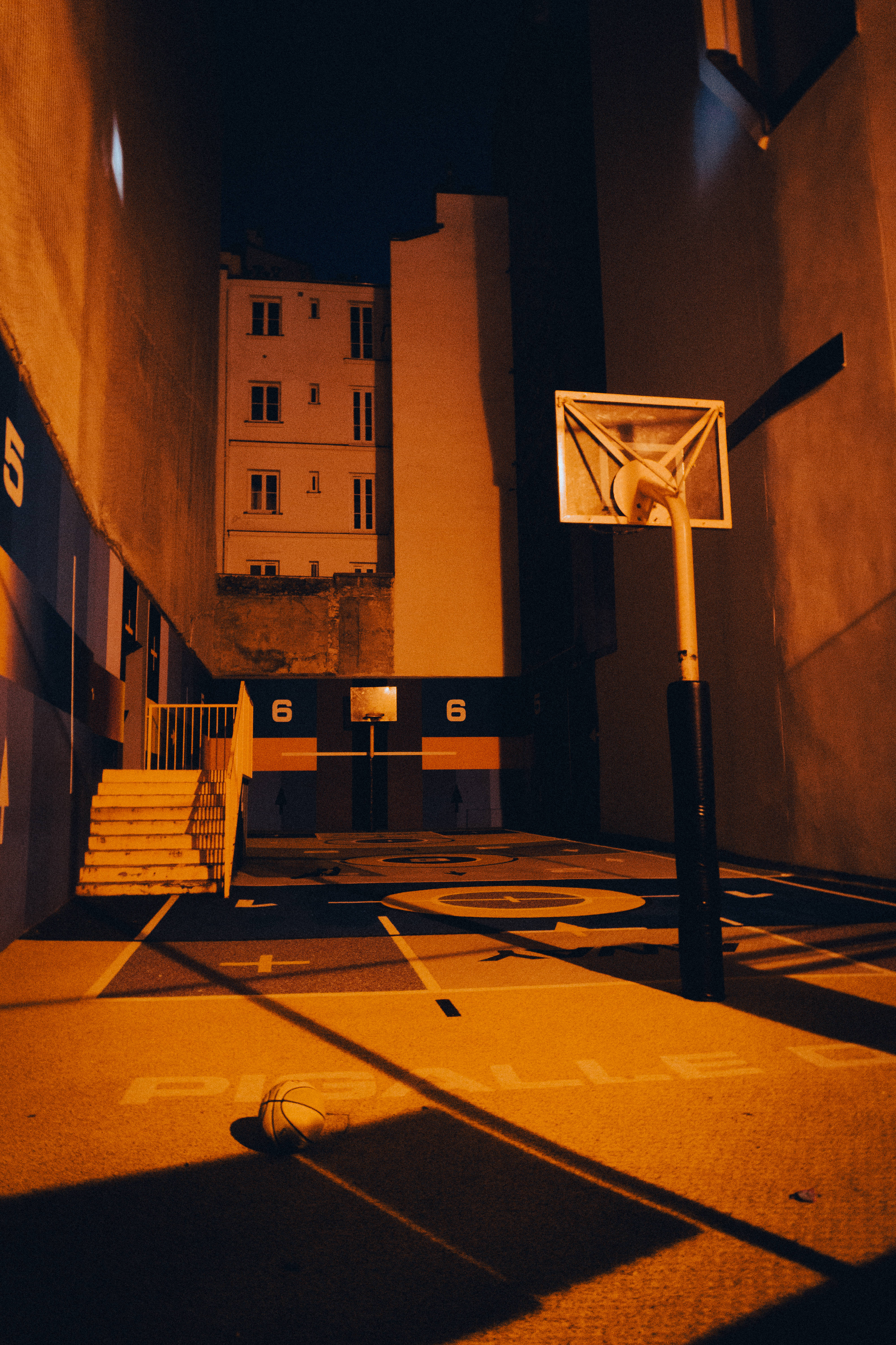 Playground 桌布 壁紙 — 夜晚昏暗的城市籃球場，沐浴在溫暖的橙色光芒中，地上放著一個籃球。