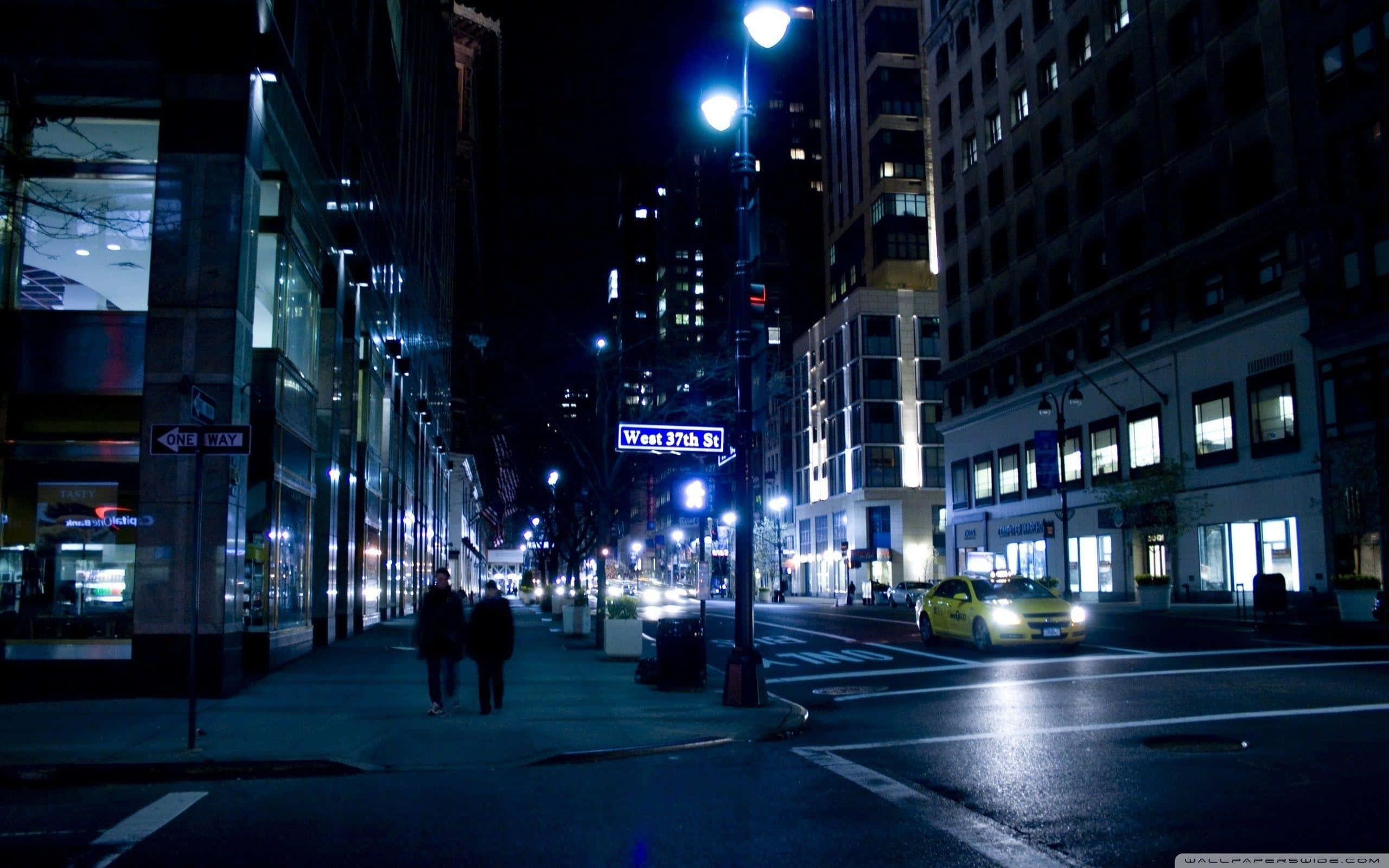 夜景城市 桌布 壁紙 — 夜晚昏暗的城市街道，有行人行走，一輛黃色的士在閃爍的路燈下駛過。