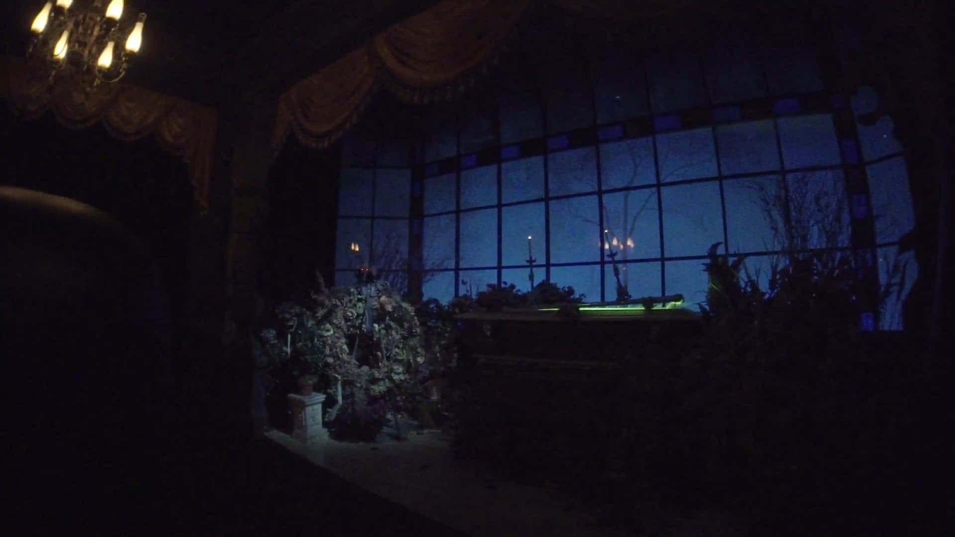 Scary Zoom 桌布 壁紙 — 夜晚昏暗的豪華房間，有吊燈和大窗戶，露出深藍色的天空和光禿禿的樹木。