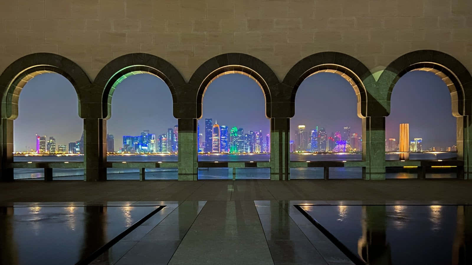 城市 桌布 壁紙 — 夜晚景色，一排拱形石窗框住充滿活力的城市天際線，倒映在濕漉漉的路面上。