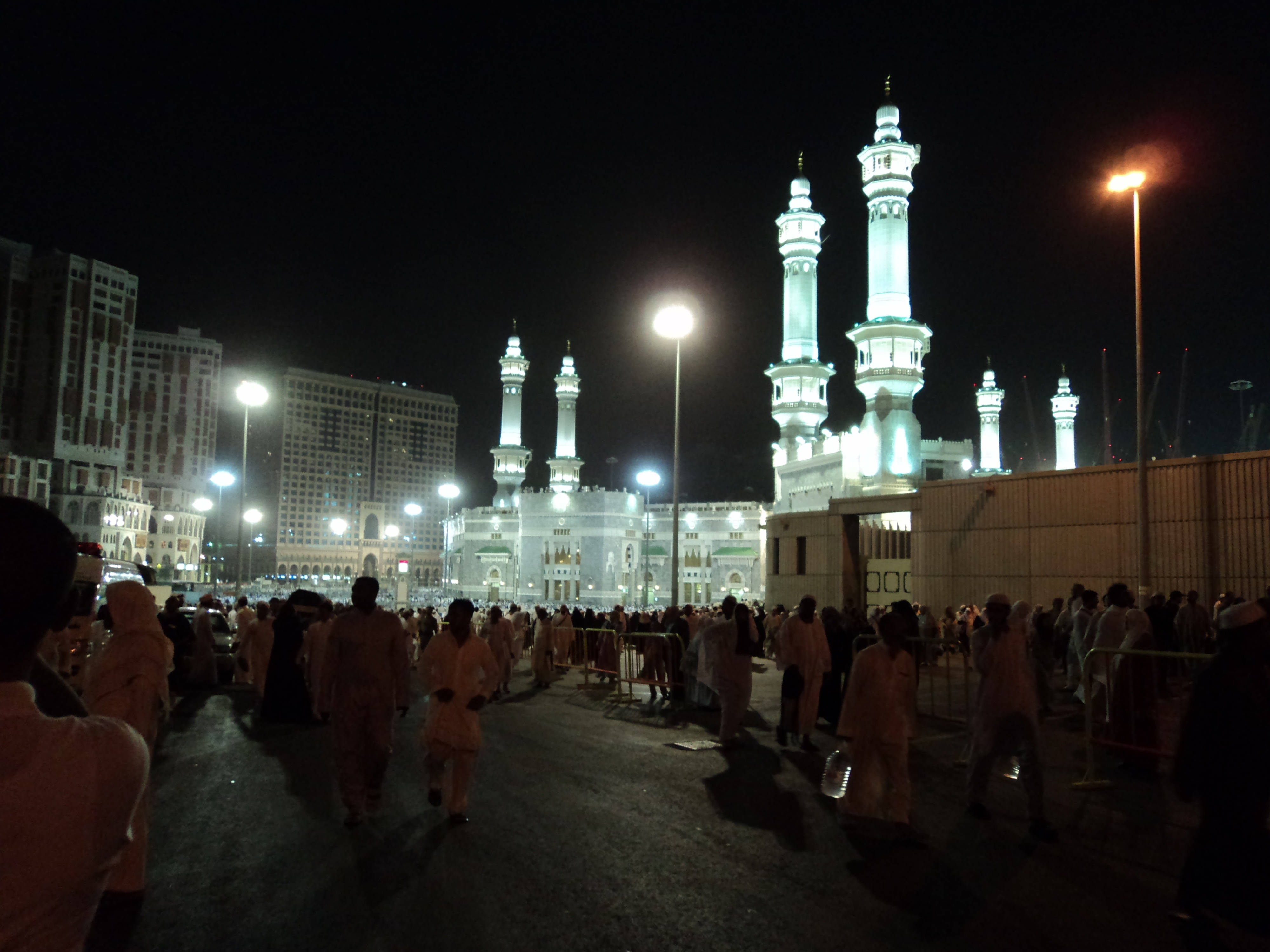 Makkah 桌布 壁紙 — 夜晚景色，清真寺燈火通明，高聳的宣禮塔，朝聖者人群在街燈下行走。