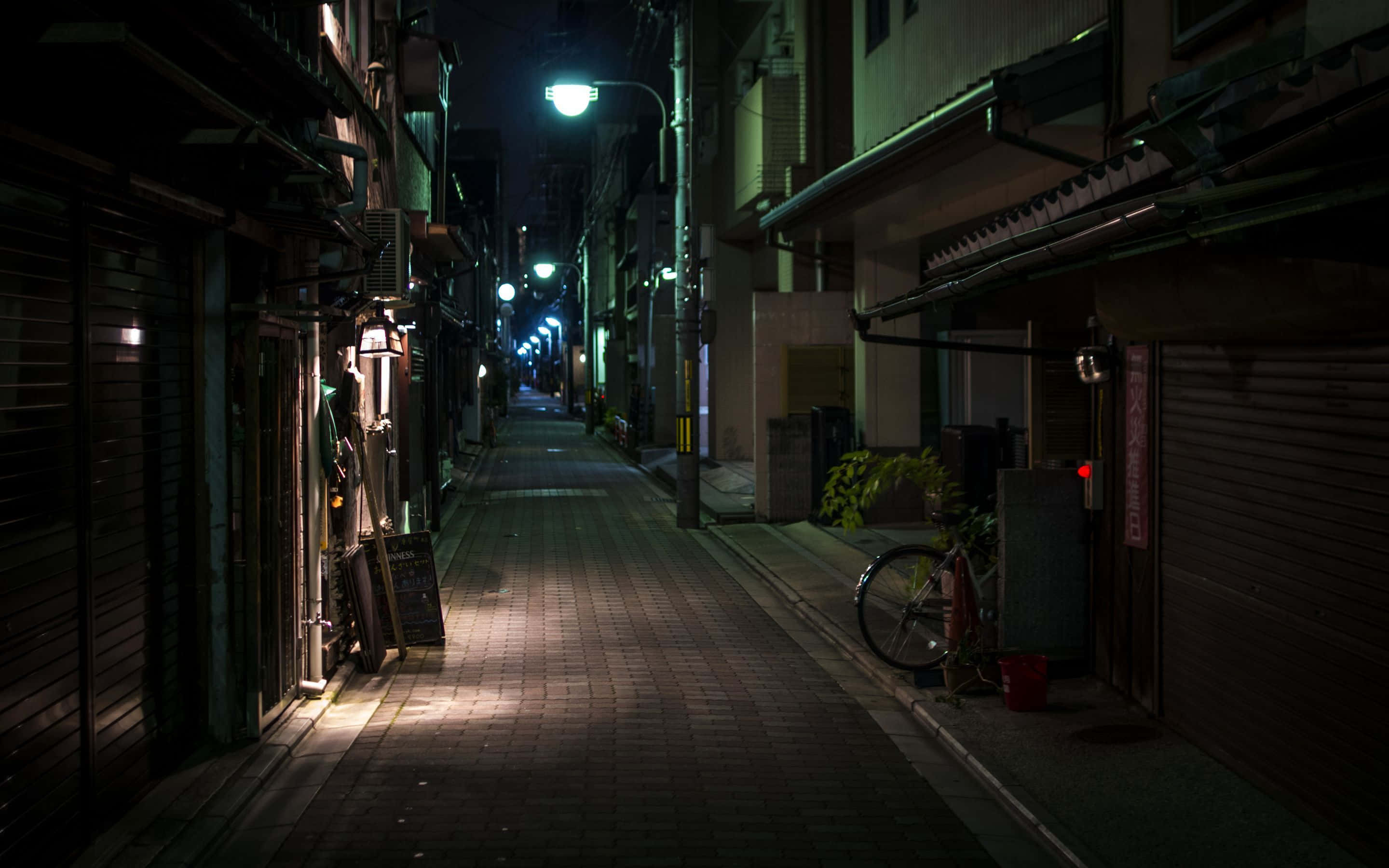 Night Street 桌布 壁紙 — 夜晚東京一條狹窄小巷，街燈照亮，在磚砌路面上投下長長的影子。