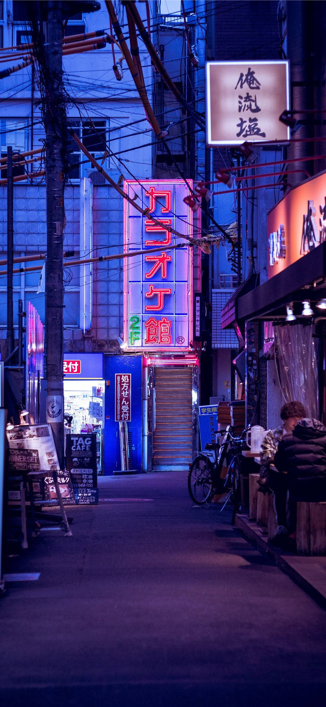 日本 桌布 壁紙 — 夜晚東京一條狹窄小巷，被發光招牌和街燈的霓虹粉紅、藍色和橙色光芒籠罩。