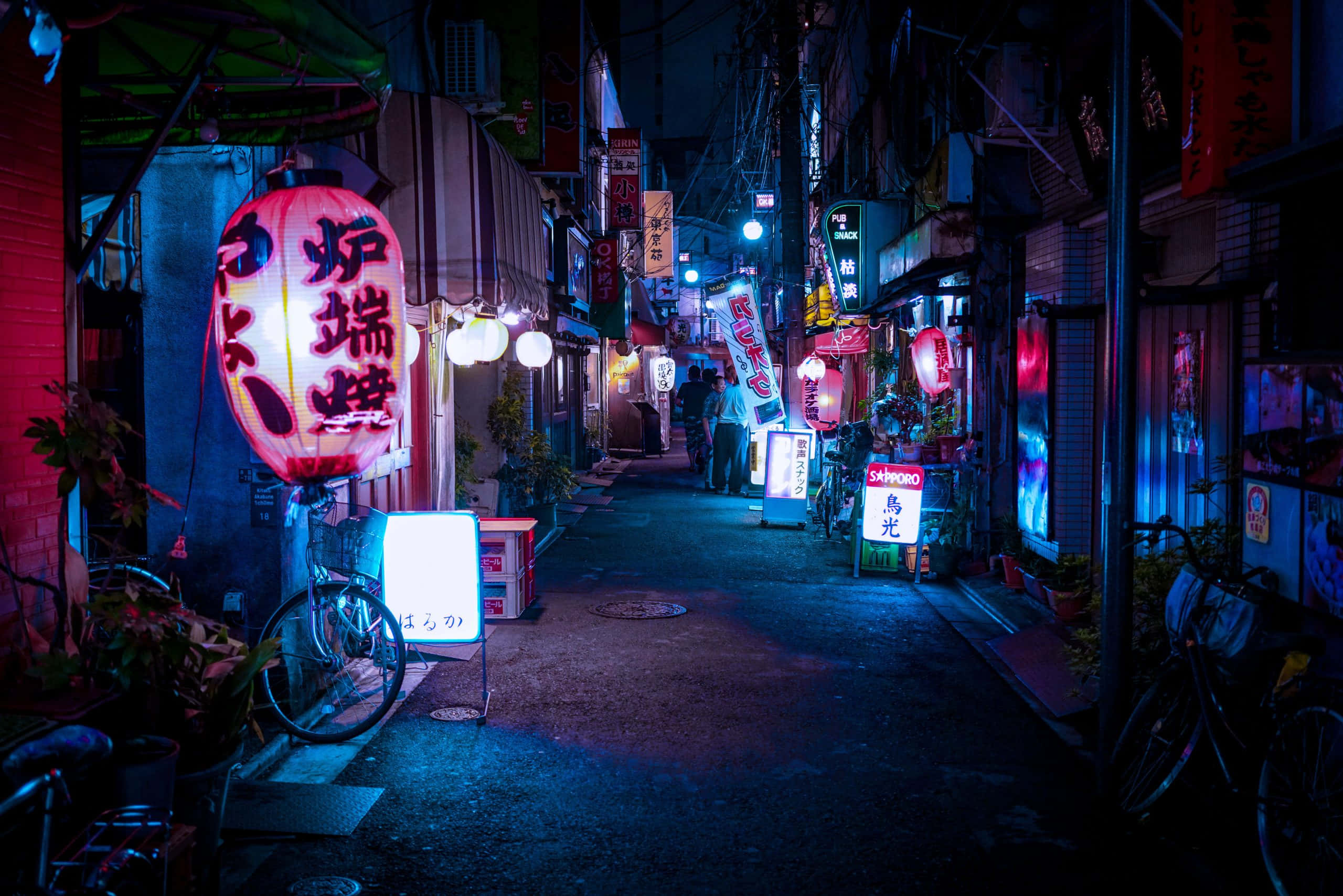 Alleyway 桌布 壁紙 — 夜晚東京一條狹窄小巷，被發光的紅色和藍色霓虹燈招牌及燈籠照亮，在潮濕的路面上投射出色彩繽紛的倒影。