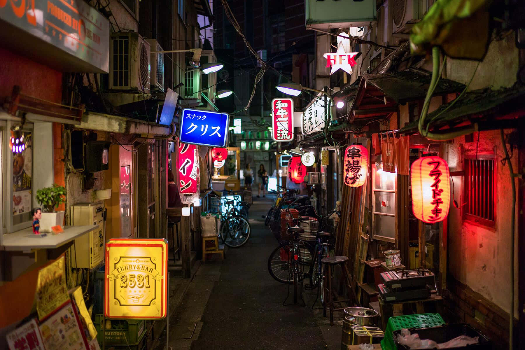 Tokyo Japan 桌布 壁紙 — 夜晚東京一條狹窄小巷，被發光的霓虹招牌和紅色燈籠照亮，腳踏車停放在風化的牆壁旁。