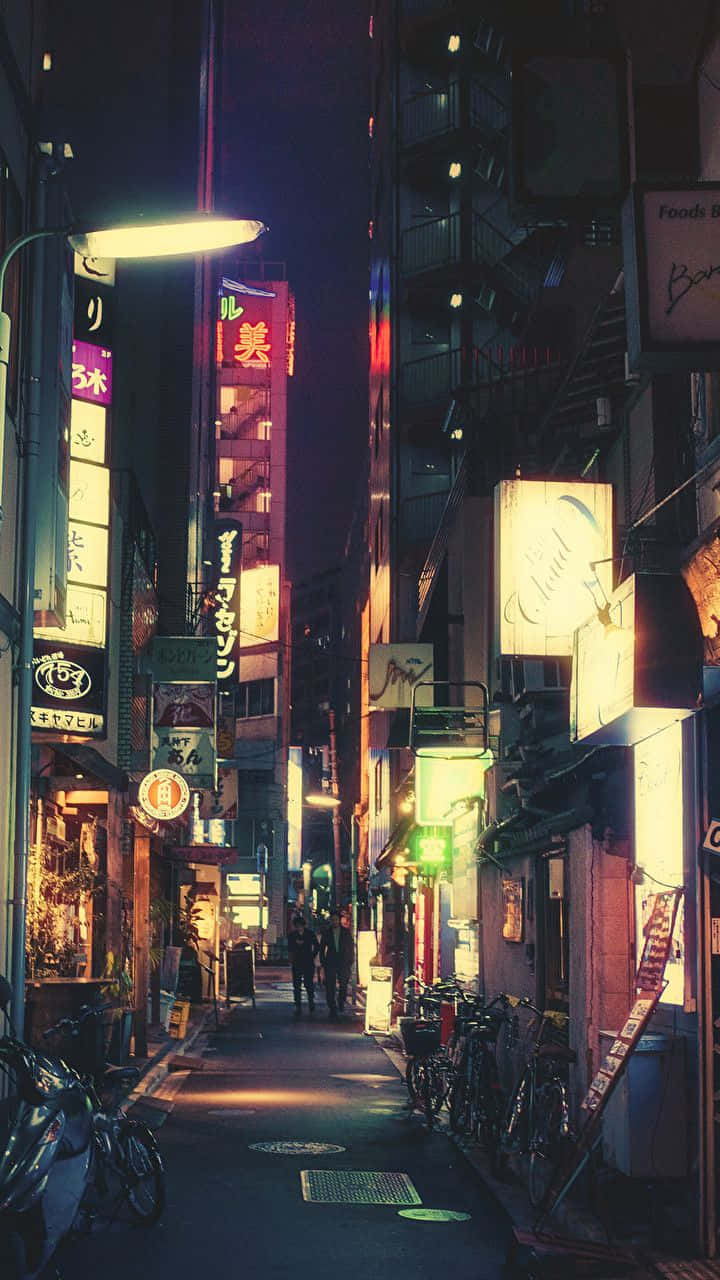 Japanese Phone 桌布 壁紙 — 夜晚東京一條狹窄的小巷，被發光的霓虹燈招牌和街燈照亮，在潮濕的路面上投射出溫暖的倒影。