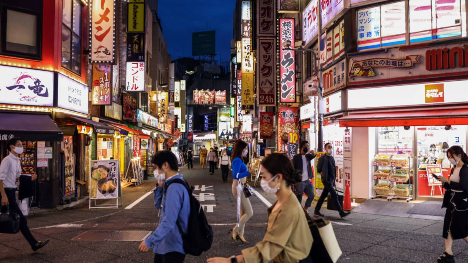 Coronavirus 桌布 壁紙 — 夜晚東京一條繁忙的霓虹燈小巷，戴著口罩的行人走過發光的招牌和商店櫥窗。