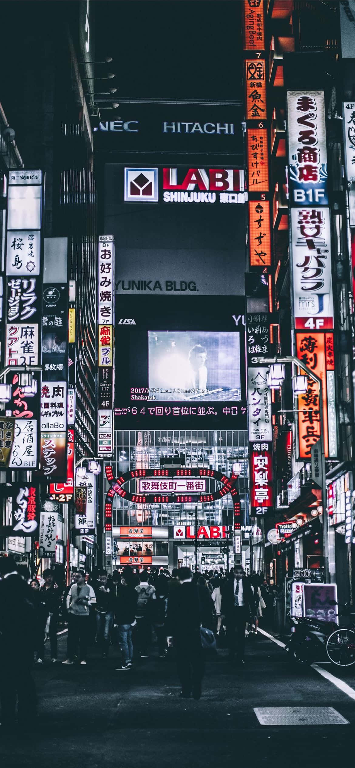 桌布 壁紙 — 夜晚東京一條繁忙的霓虹燈街道，高聳的招牌和擁擠的人群。