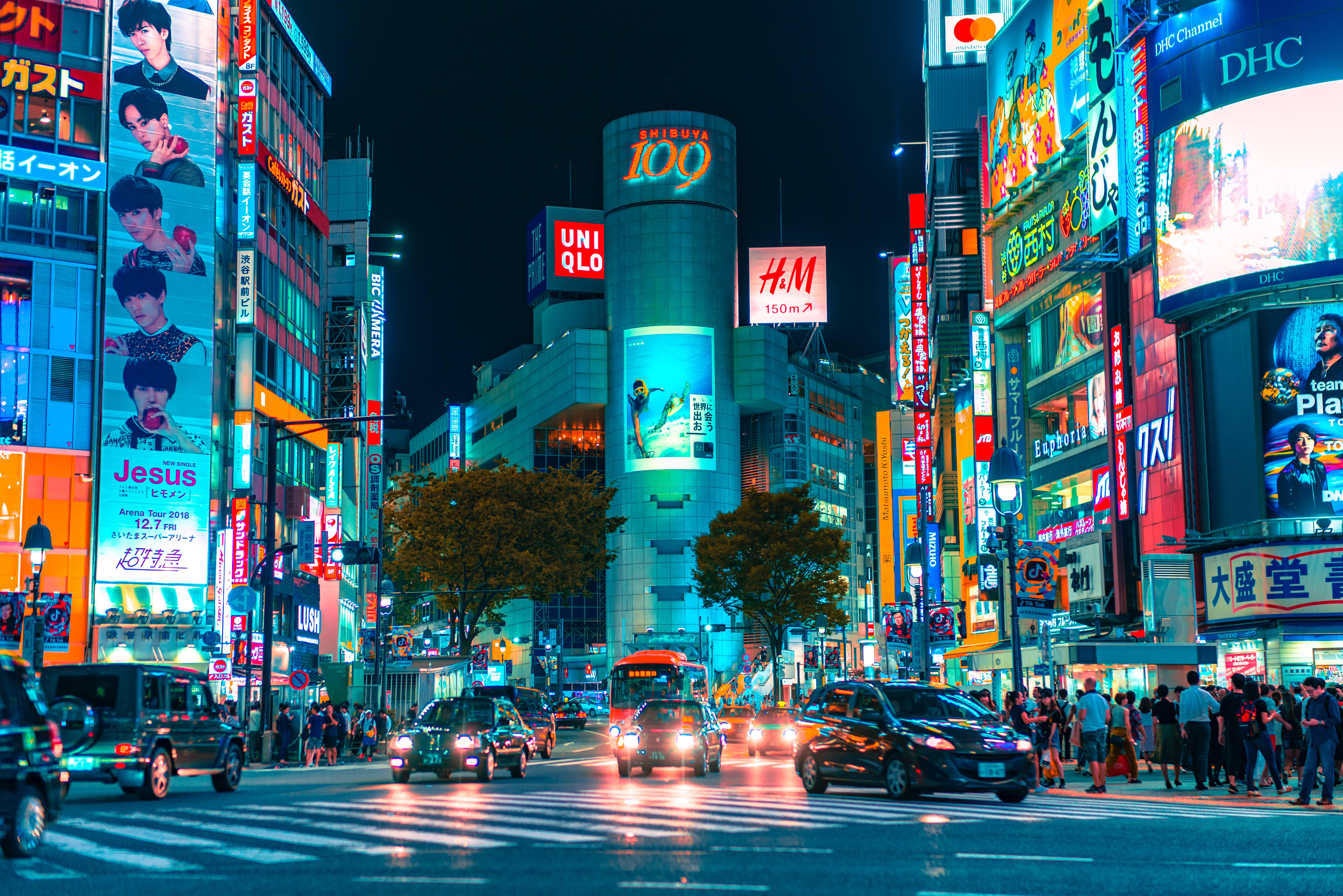 日本 桌布 壁紙 — 夜晚東京一條耀眼的霓虹燈街道，高聳的廣告牌在繁忙的交通和行人上方閃爍。