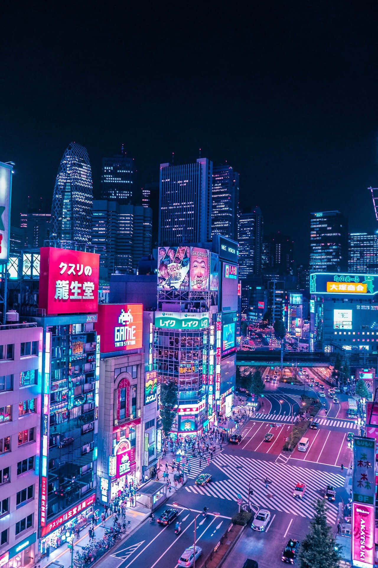 City Night 桌布 壁紙 — 夜晚東京一條耀眼的霓虹燈街道，高聳的摩天大樓閃爍著電光藍和粉紅色。