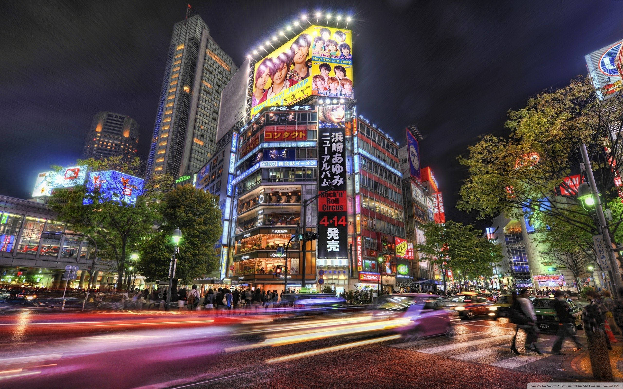 東京 桌布 壁紙 — 夜晚東京充滿活力的霓虹燈街道，模糊的車燈和人群在聳立的廣告牌下。