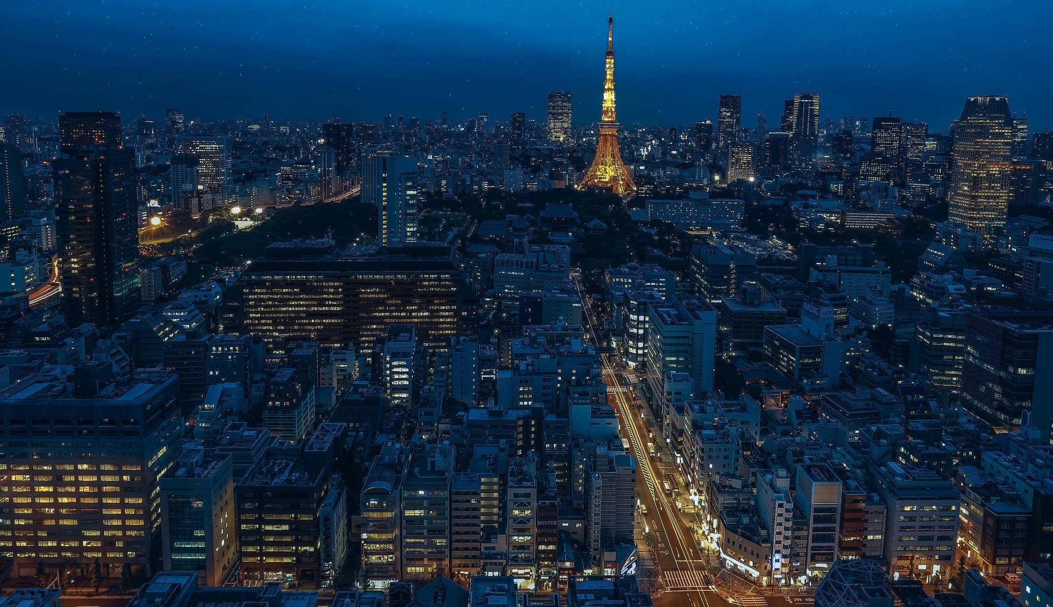 日本 桌布 壁紙 — 夜晚東京的鳥瞰圖，燈火通明的東京鐵塔聳立在密集的摩天大樓和街道構成的城市景觀之上。