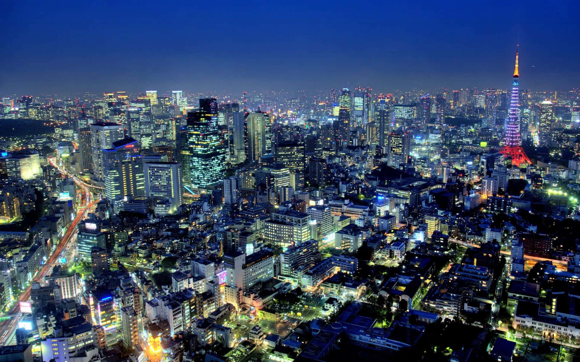 東京 桌布 壁紙 — 夜晚東京的鳥瞰圖，閃爍的摩天大樓和標誌性的東京塔在深藍色天空的映襯下熠熠生輝。