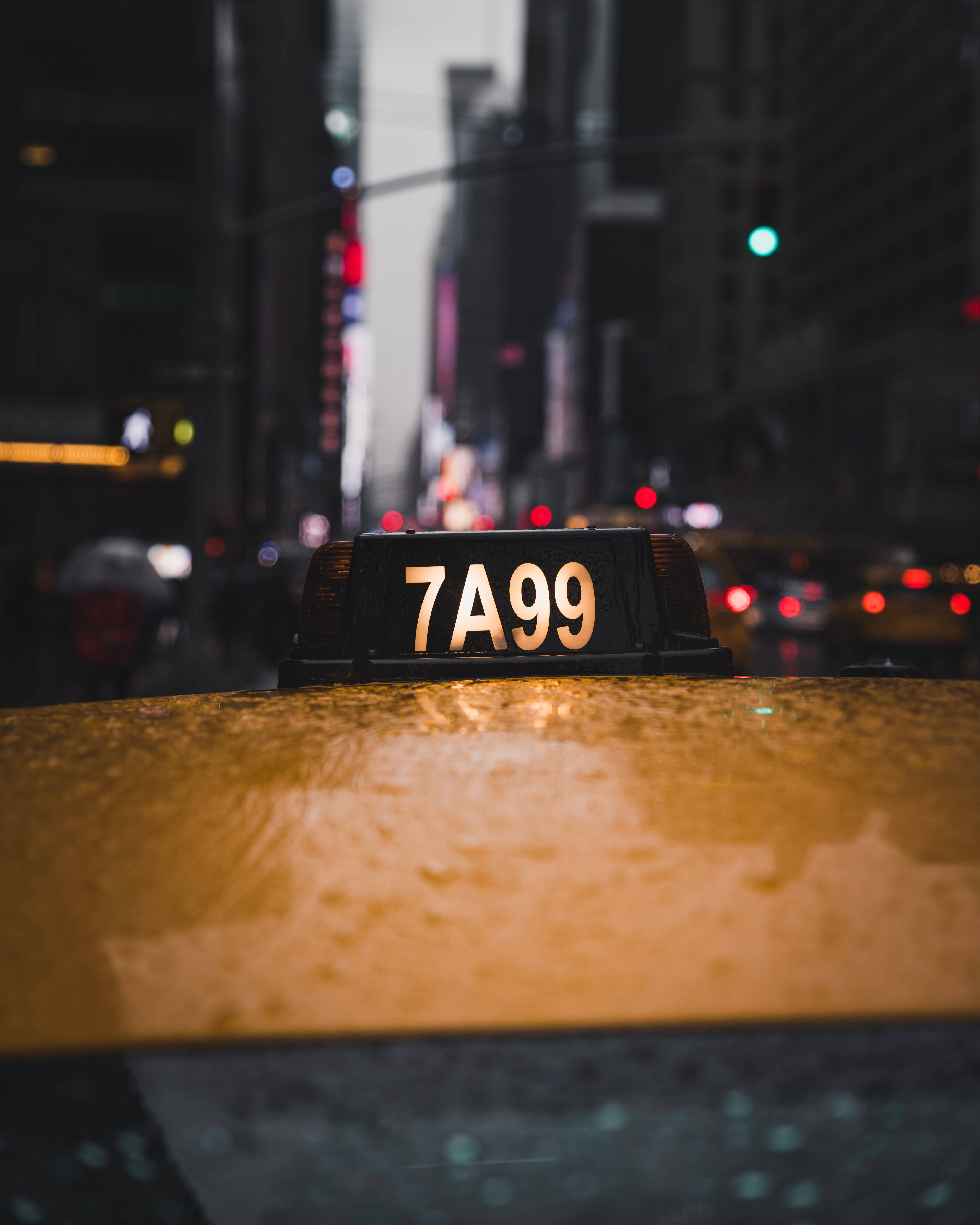 New 桌布 壁紙 — 夜晚模糊的城市街道背景下，黃色計程車車頂的特寫，上面有一個亮著的標誌寫著7A99。