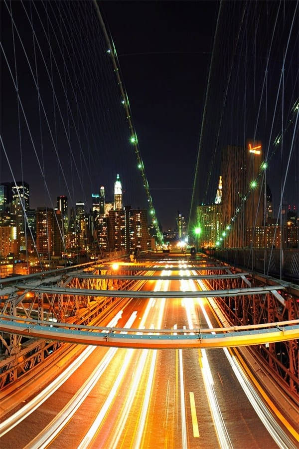 繁忙橋樑的夜景，移動車輛的光跡和背景中燈火通明的城市天際線。 — 頂級 iPhone 桌布 壁紙