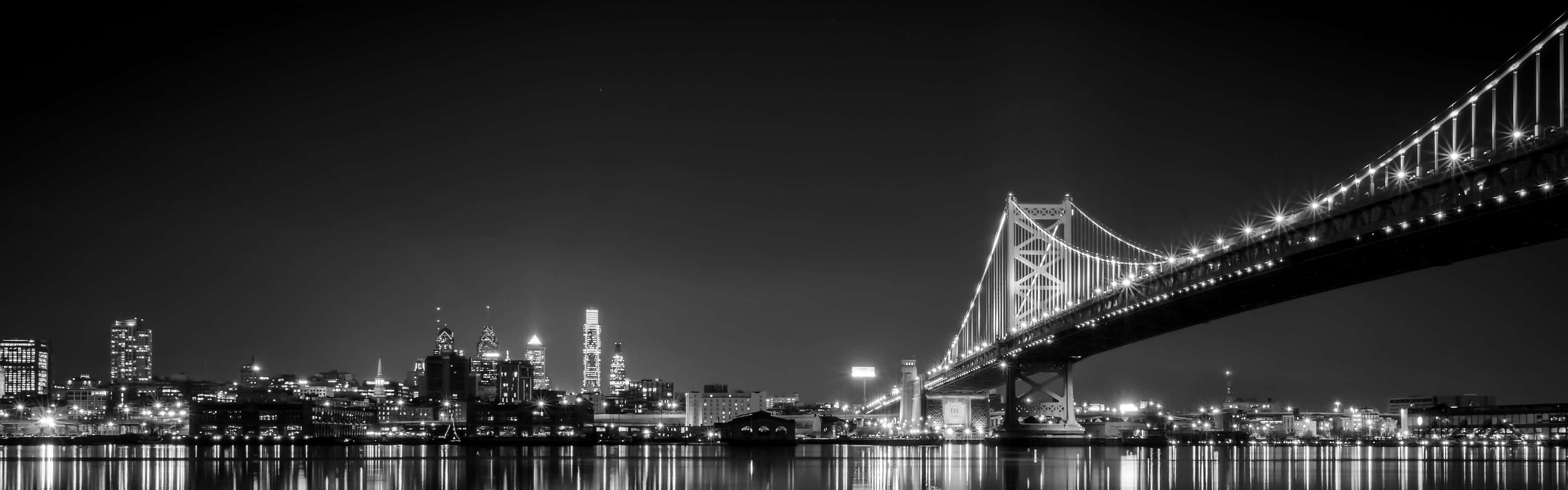 San Francisco Black And White 桌布 壁紙 — 夜晚海灣大橋和舊金山天際線的醒目黑白全景圖，城市燈光倒映在水面上。