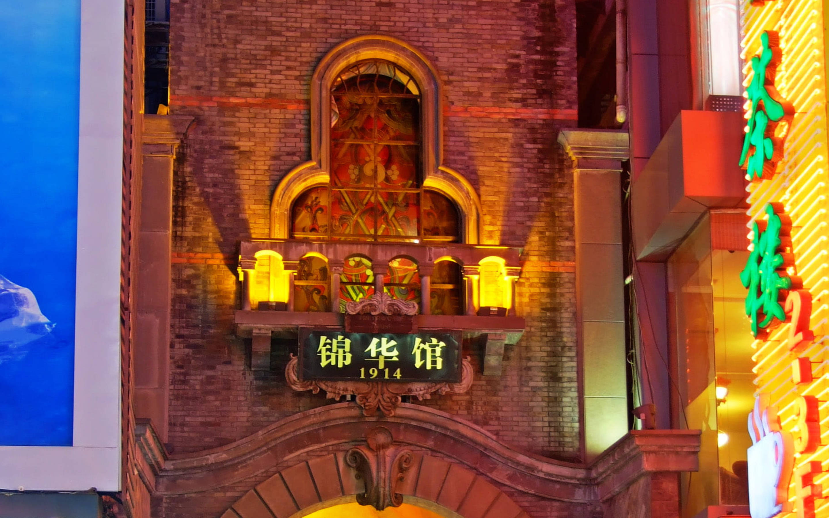 Chengdu 桌布 壁紙 — 夜晚溫暖照亮的歷史磚建築外牆，帶有發光霓虹燈招牌和裝飾性拱形窗。