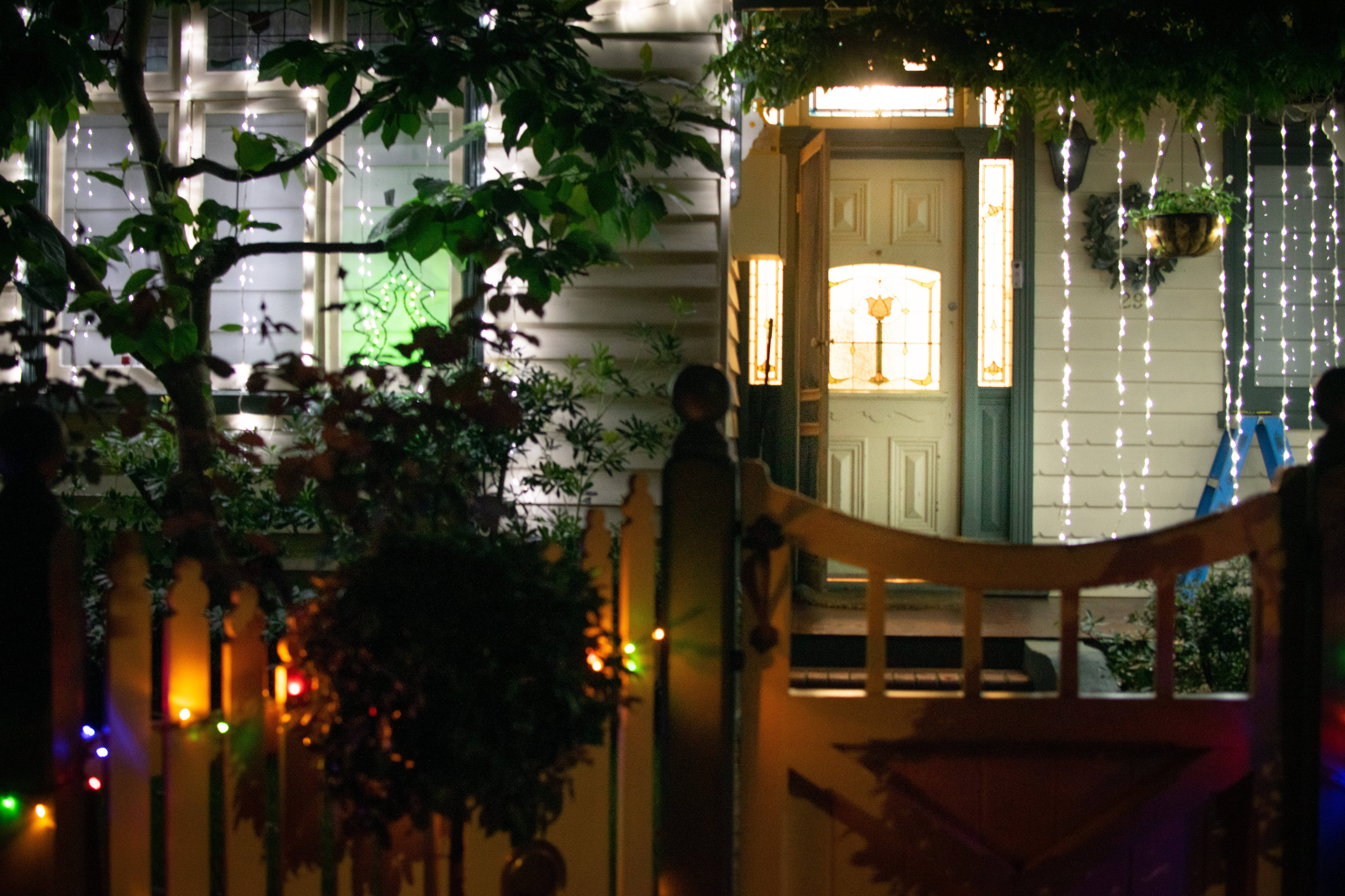 House 桌布 壁紙 — 夜晚溫暖照明的房屋入口，裝飾著串燈和綠植，由木門框住。