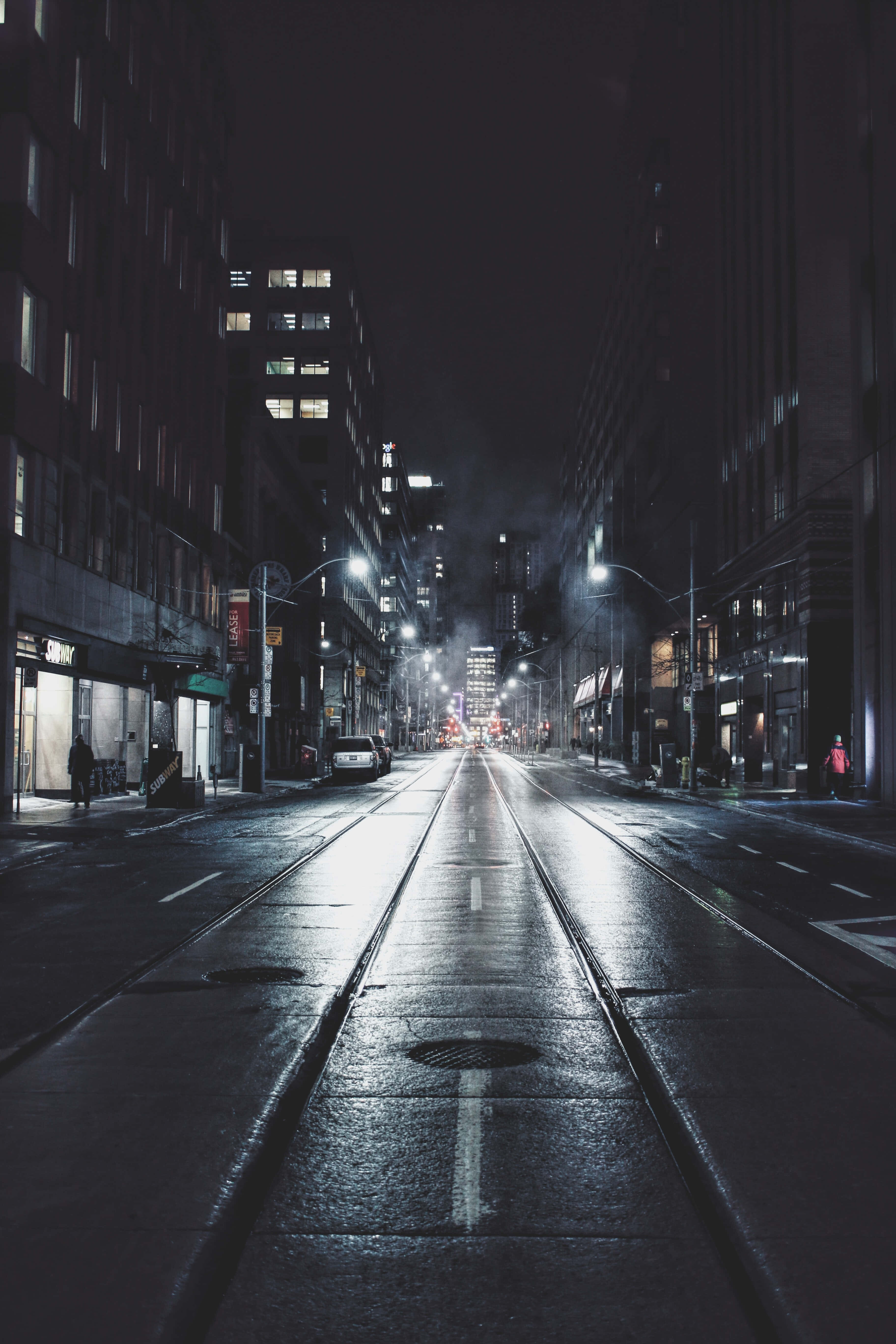 Street 桌布 壁紙 — 夜晚潮濕的城市街道反射著街燈和建築物窗戶，營造出陰鬱的城市峽谷。