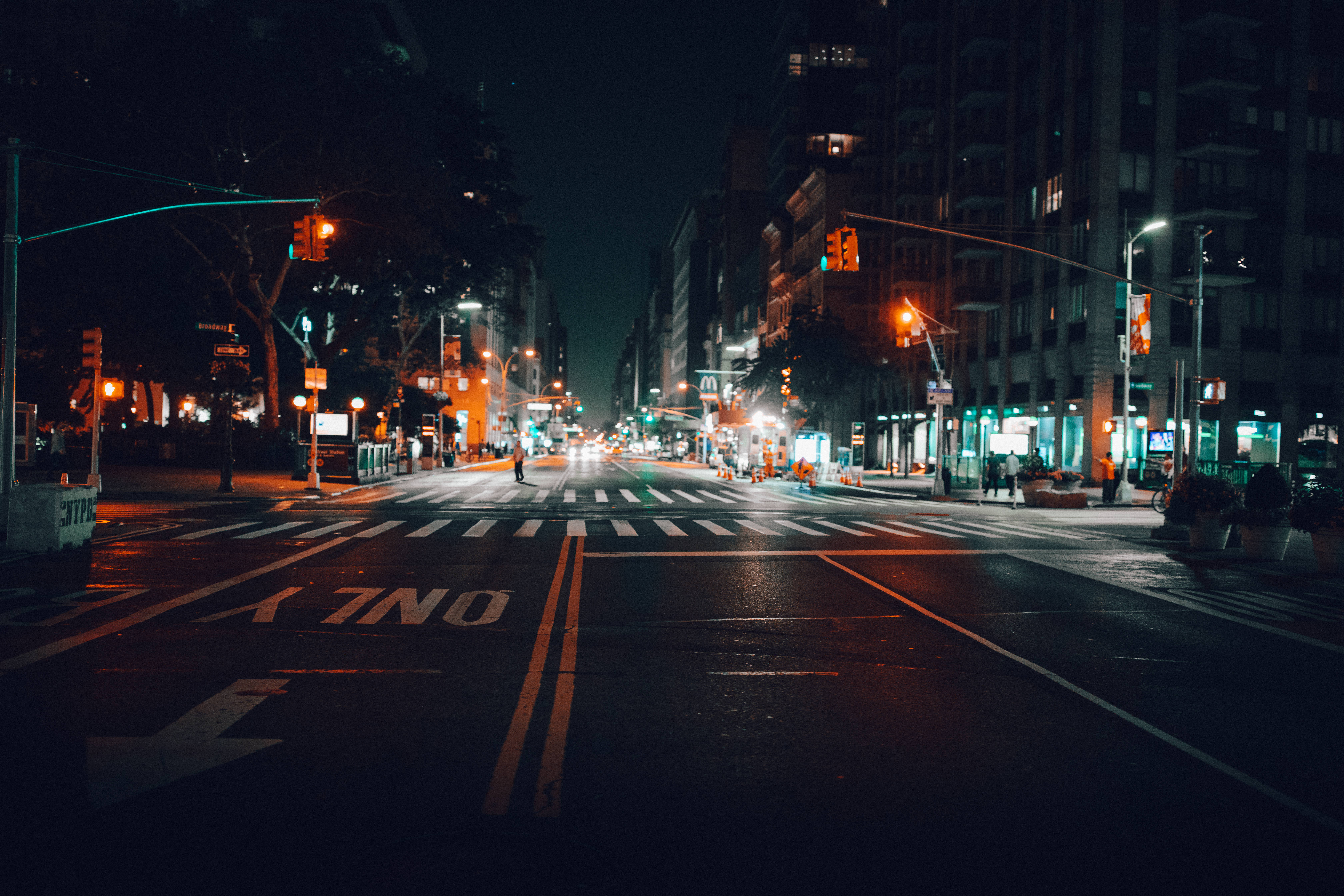 New 桌布 壁紙 — 夜晚濕漉漉的城市街道，在高聳的建築物下反射出橙色的交通燈和遠處的車頭燈。
