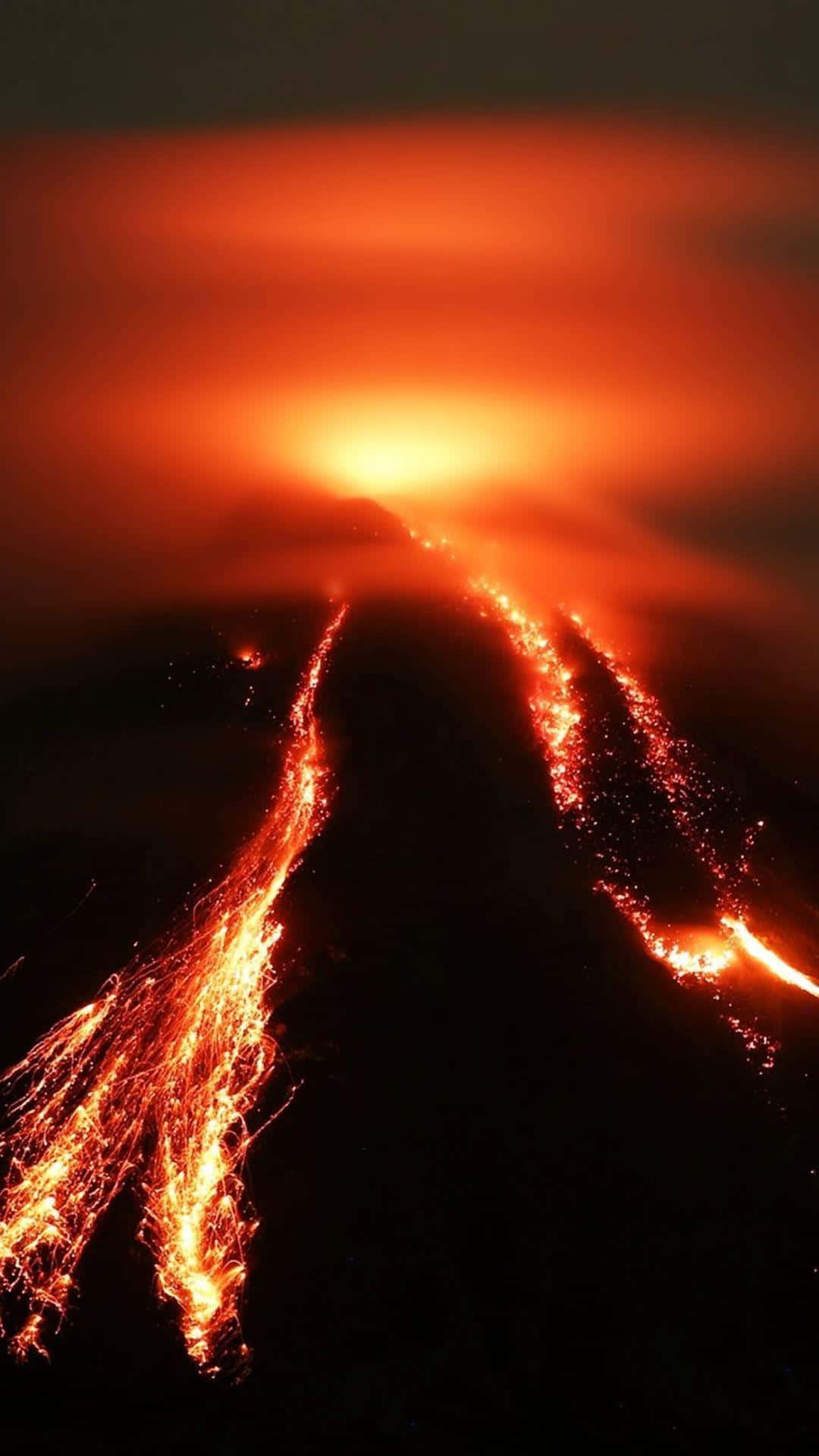 自然 桌布 壁紙 — 夜晚火山爆發，發光的熔岩河流在橙色天空下沿著黑暗的山坡流下。