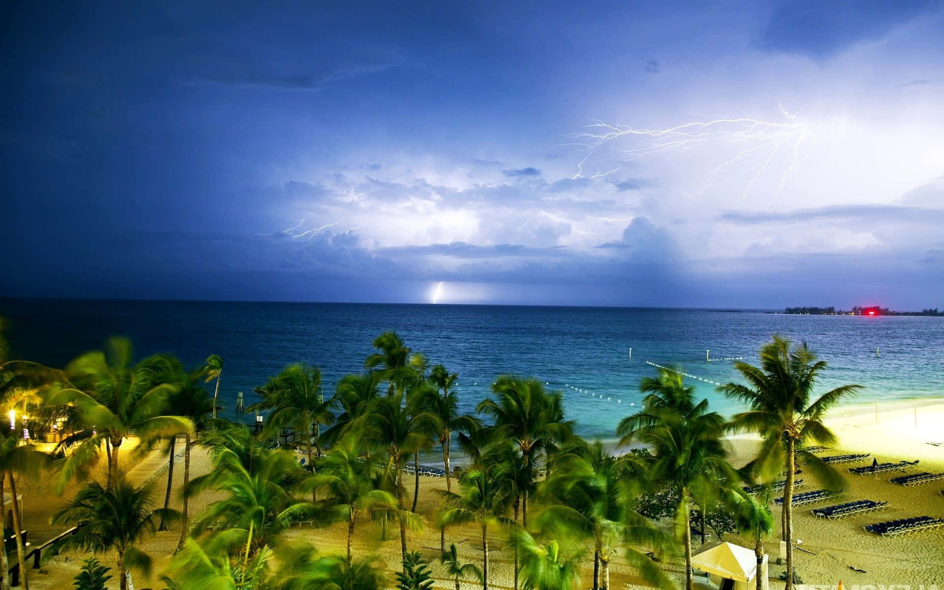Bahamas Beach 桌布 壁紙 — 夜晚熱帶海灘的戲劇性場景，閃電照亮海洋和棕櫚樹上方的烏雲。