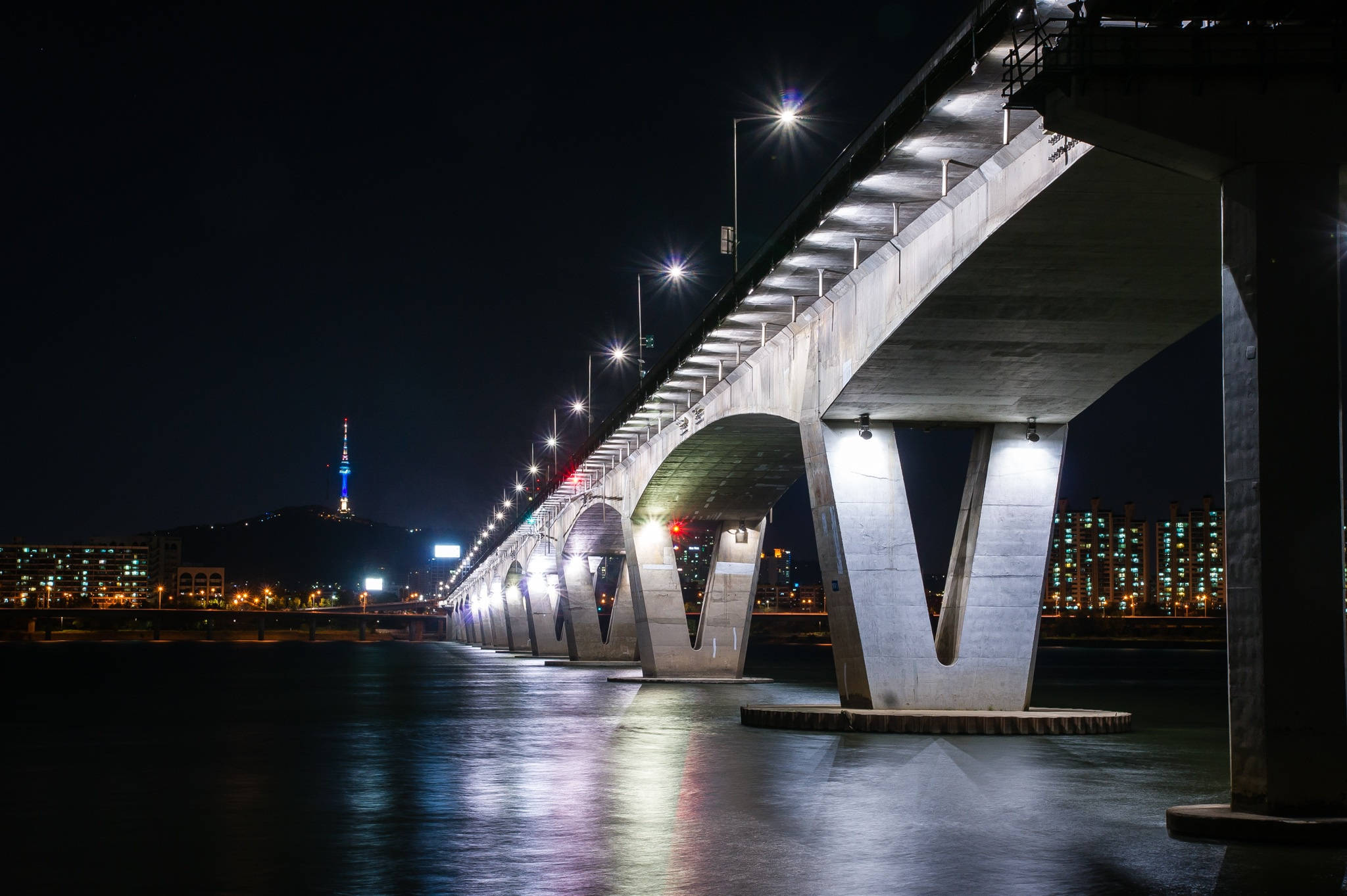 南韓 桌布 壁紙 — 夜晚燈光璀璨的宏偉混凝土橋樑，城市燈光倒映在下方平靜的水面上。