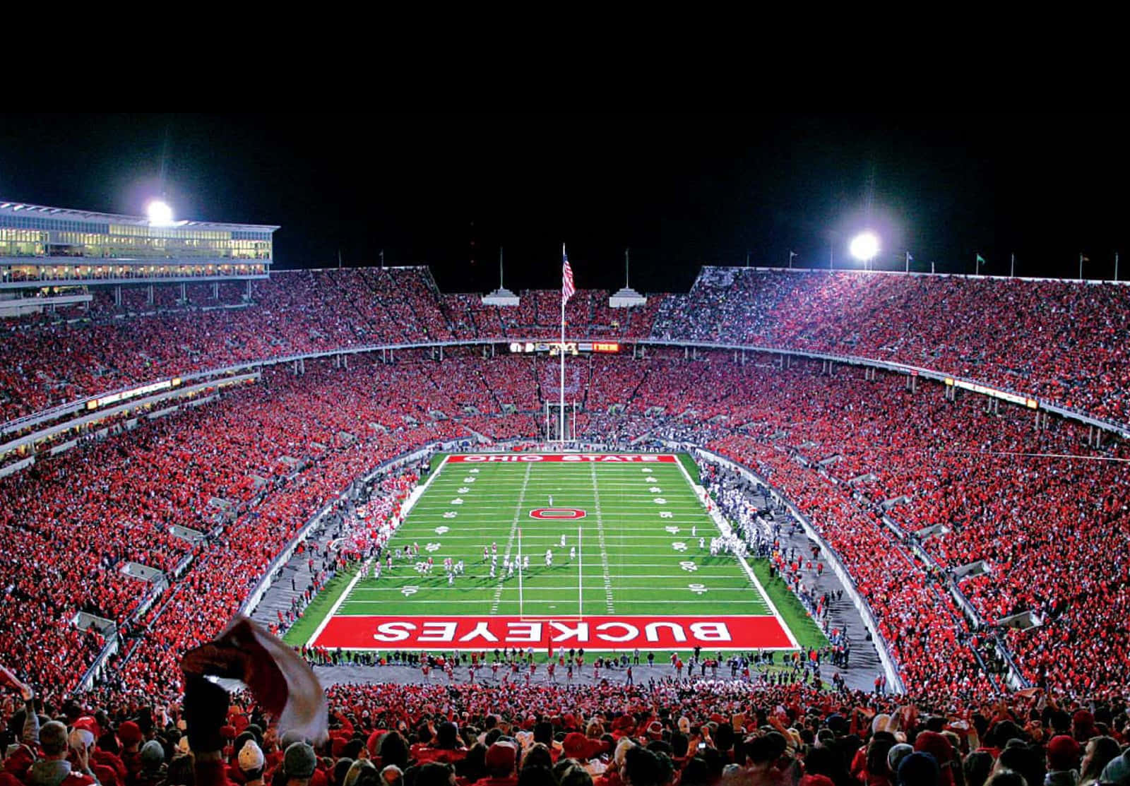 Cool Ohio State 桌布 壁紙 — 夜晚燈光璀璨的足球場座無虛席，身穿紅衣的球迷在歡呼，球員們在場上列隊。