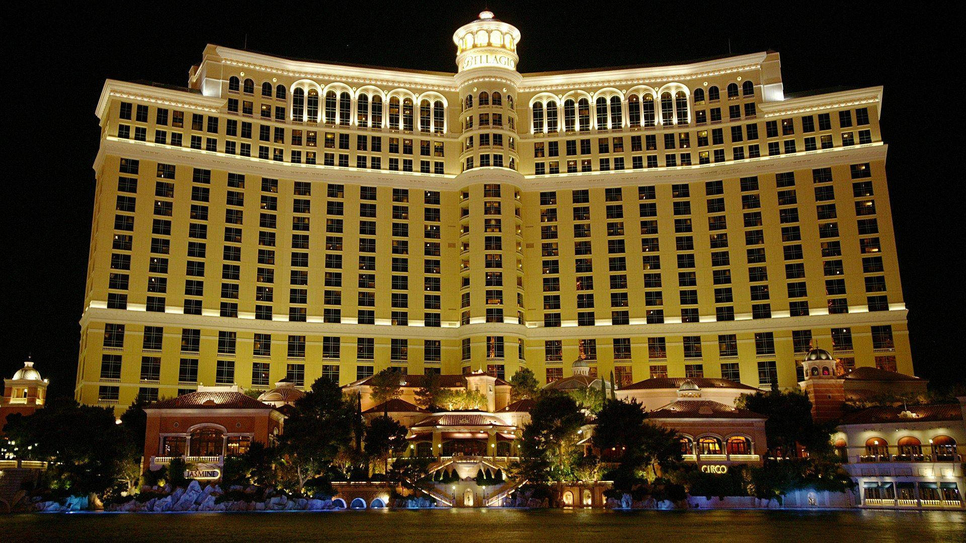 Las Vegas 桌布 壁紙 — 夜晚燈火通明的宏偉金色酒店賭場，發光的窗戶和華麗的建築倒映在平靜的水面上。