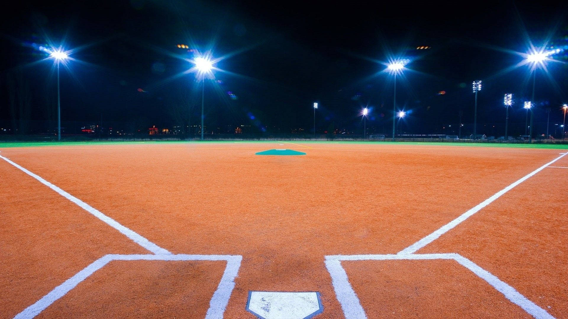Athletic 桌布 壁紙 — 夜晚燈火通明的棒球場，體育場燈光照亮泥土內野和白色界線。