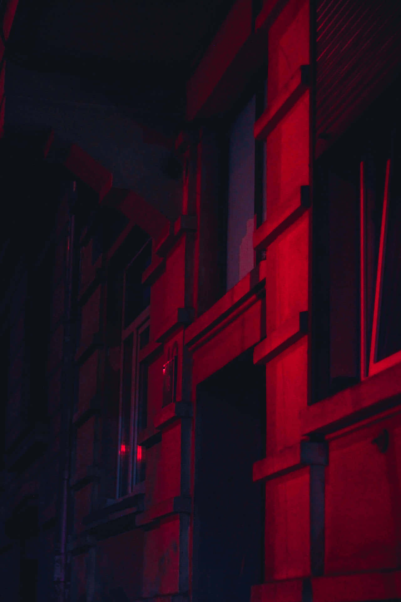 Dark Red Aesthetic 桌布 壁紙 — 夜晚狹窄的城市小巷，沐浴在強烈的紅色霓虹燈光中，在紋理磚牆上投射出戲劇性的陰影。