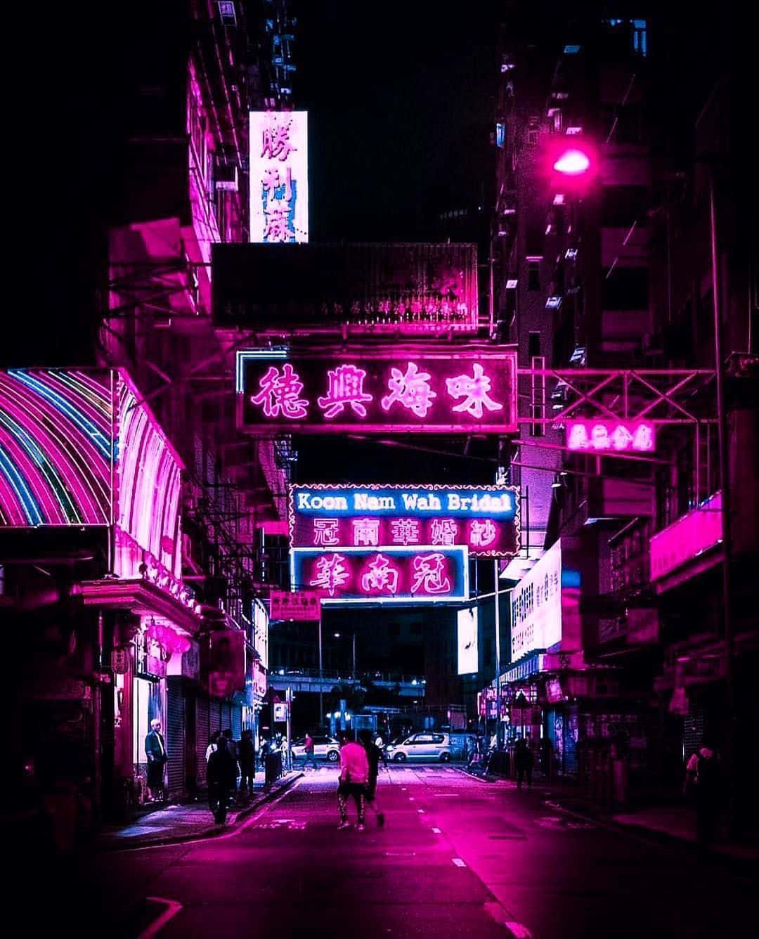 桌布 壁紙 — 夜晚狹窄的城市小巷，沐浴在鮮豔的粉紅色霓虹燈招牌中，倒映在濕漉漉的人行道上，行人在下方行走。