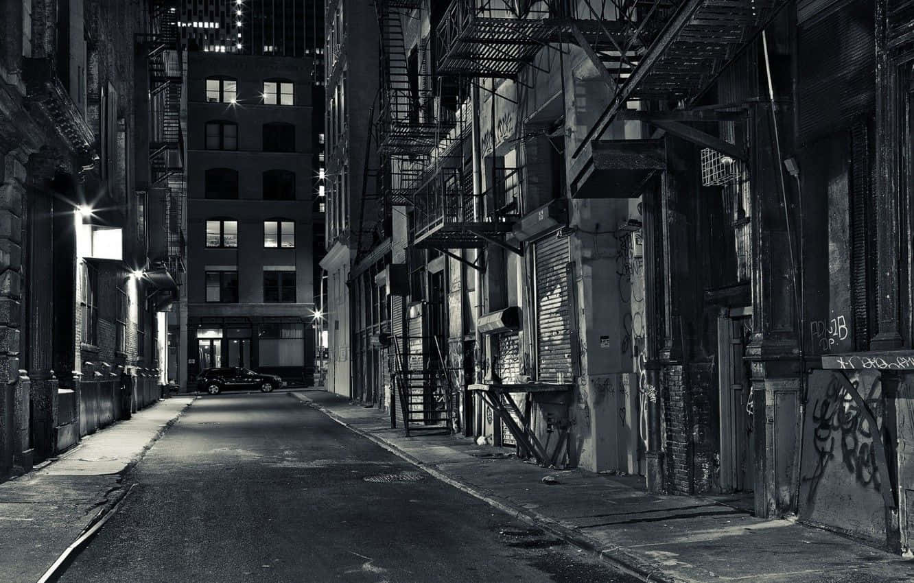 Black And White Street 桌布 壁紙 — 夜晚狹窄的城市小巷，牆上佈滿塗鴉，有防火梯，一輛孤獨的汽車停在街燈下。