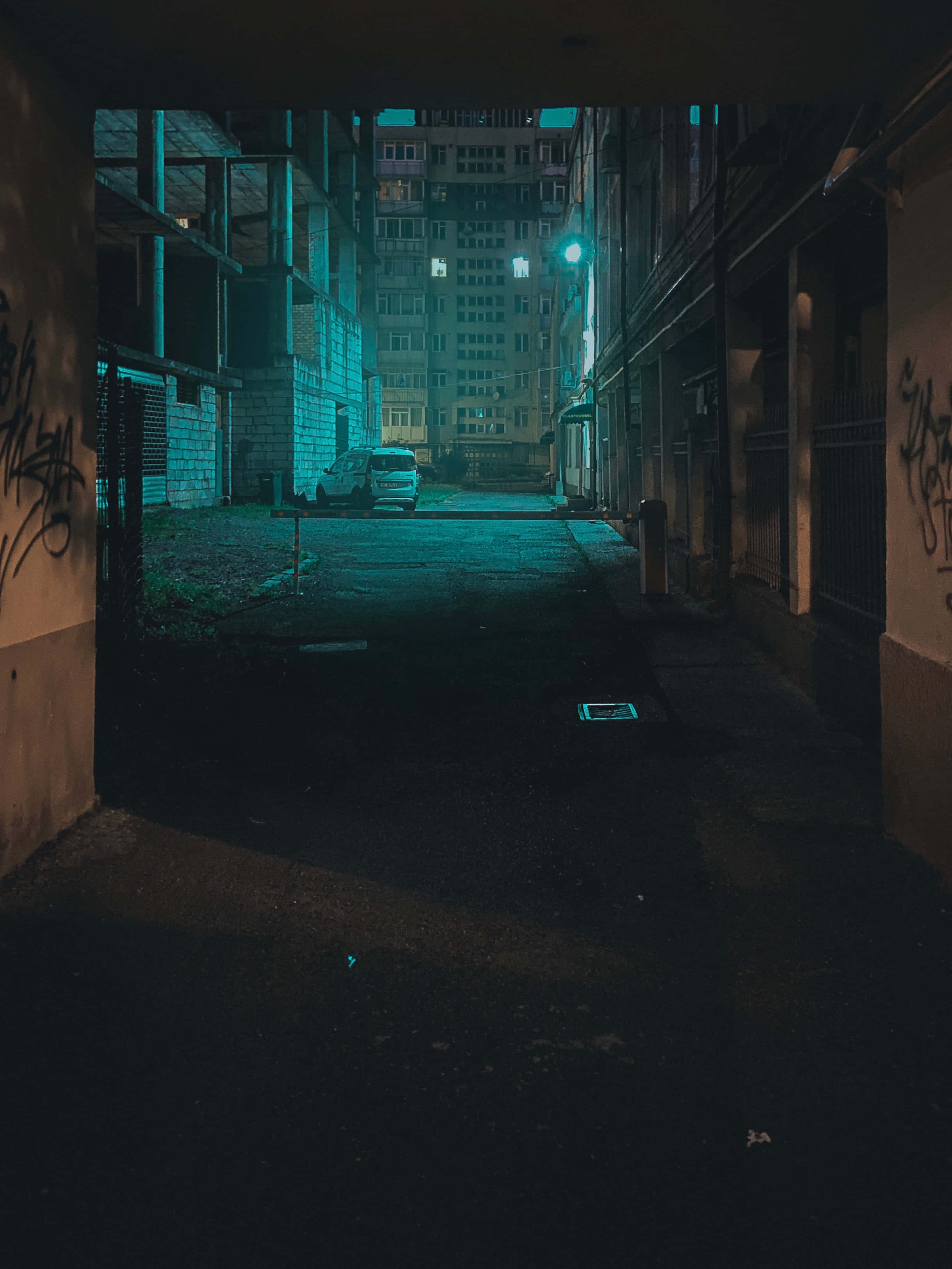 Alleyway 桌布 壁紙 — 夜晚狹窄的城市小巷，被單一街燈的詭異青綠色光芒籠罩，牆上有塗鴉，遠處停著一輛孤獨的汽車。
