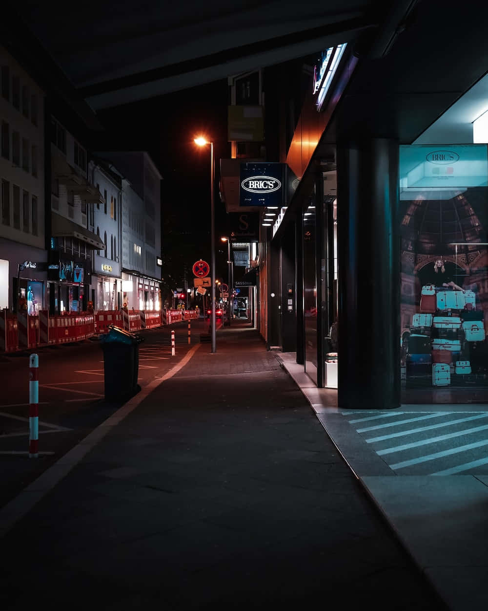 Night Street 桌布 壁紙 — 夜晚狹窄的城市小巷，被溫暖的路燈和發光的商店招牌照亮，在潮濕的人行道上投下長長的影子。
