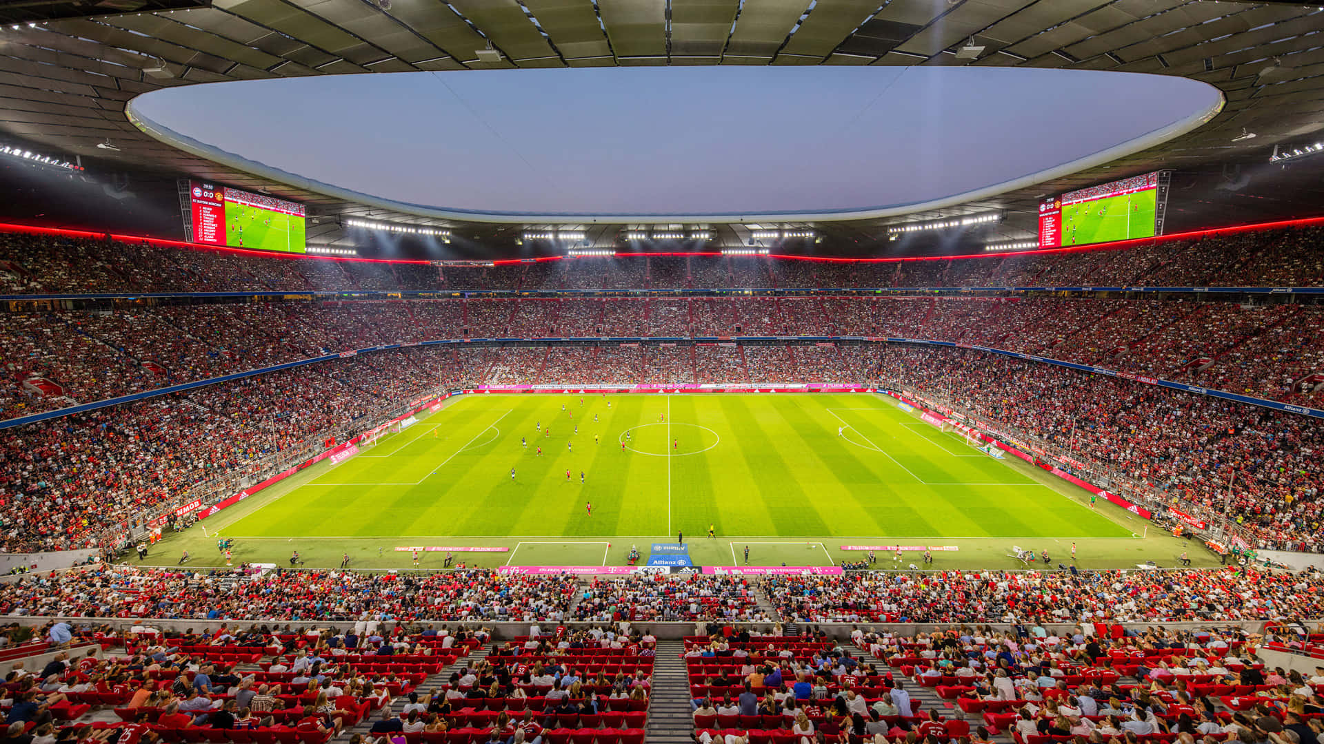 Soccer Stadium 桌布 壁紙 — 夜晚現代屋頂下，一個擠滿人的足球場的鳥瞰圖，擁有充滿活力的綠色草坪和紅色座位。