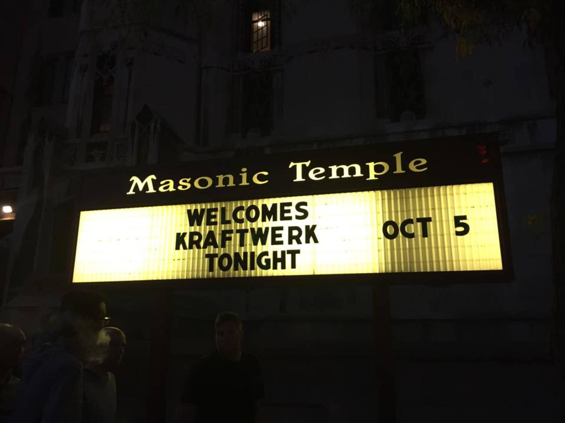 band 桌布 壁紙 — 夜晚發光的招牌宣佈 Kraftwerk 於10月5日在共濟會神廟的音樂會，下方有剪影人物。